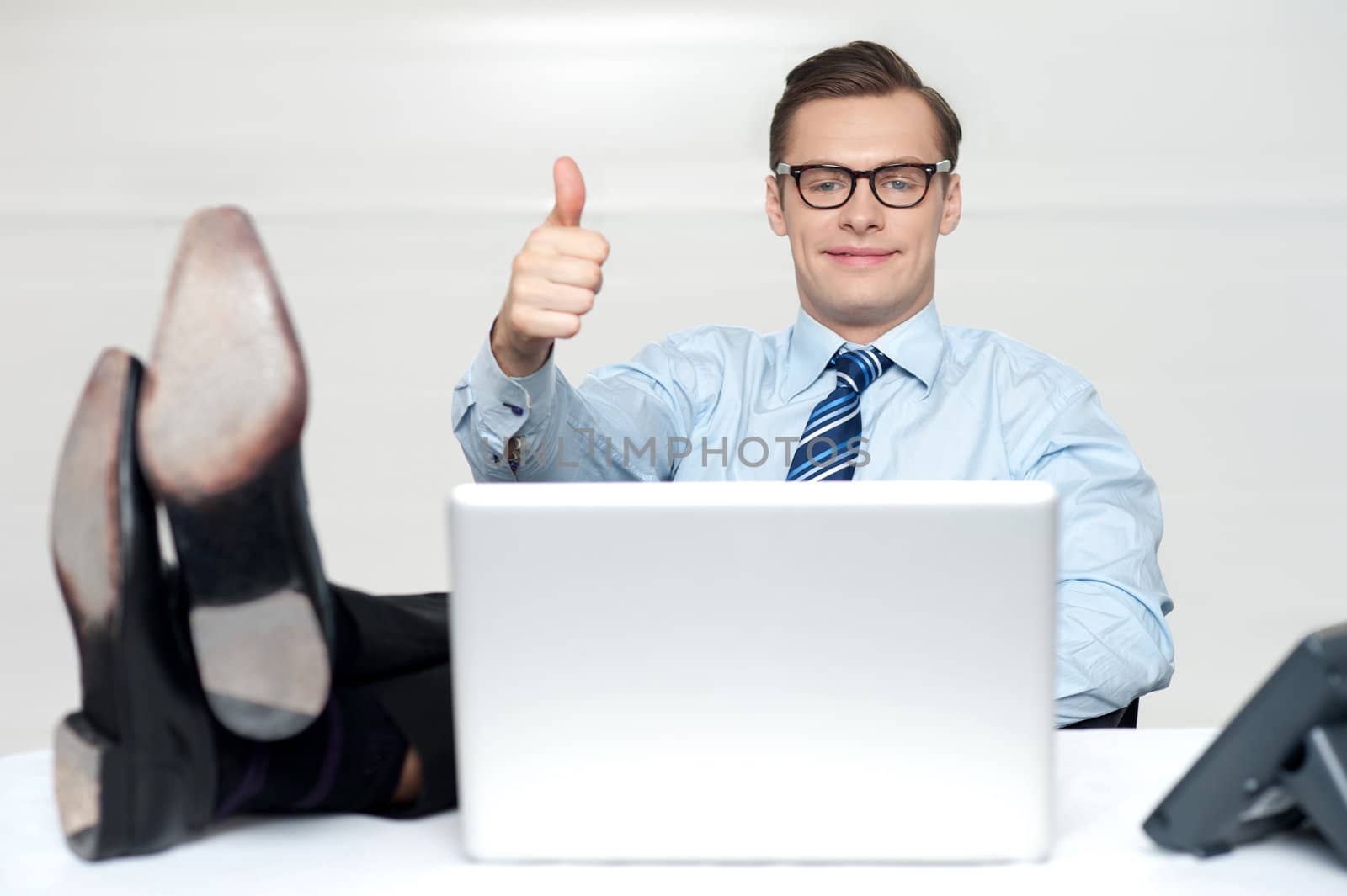 Thumbs up guy relaxing with legs on work desk. Shot in office