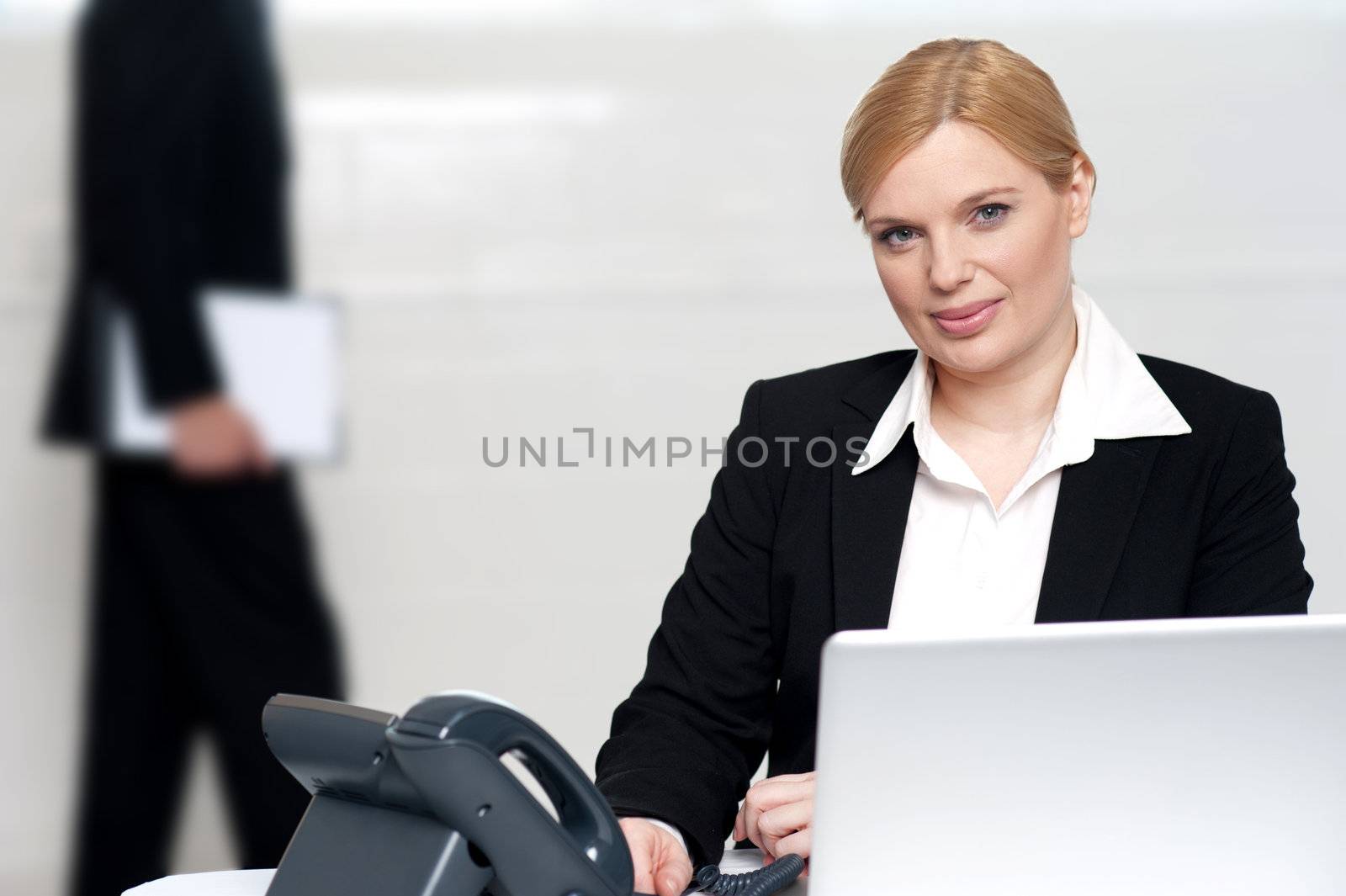 Businesswoman looking at camera while a man walking behind in background