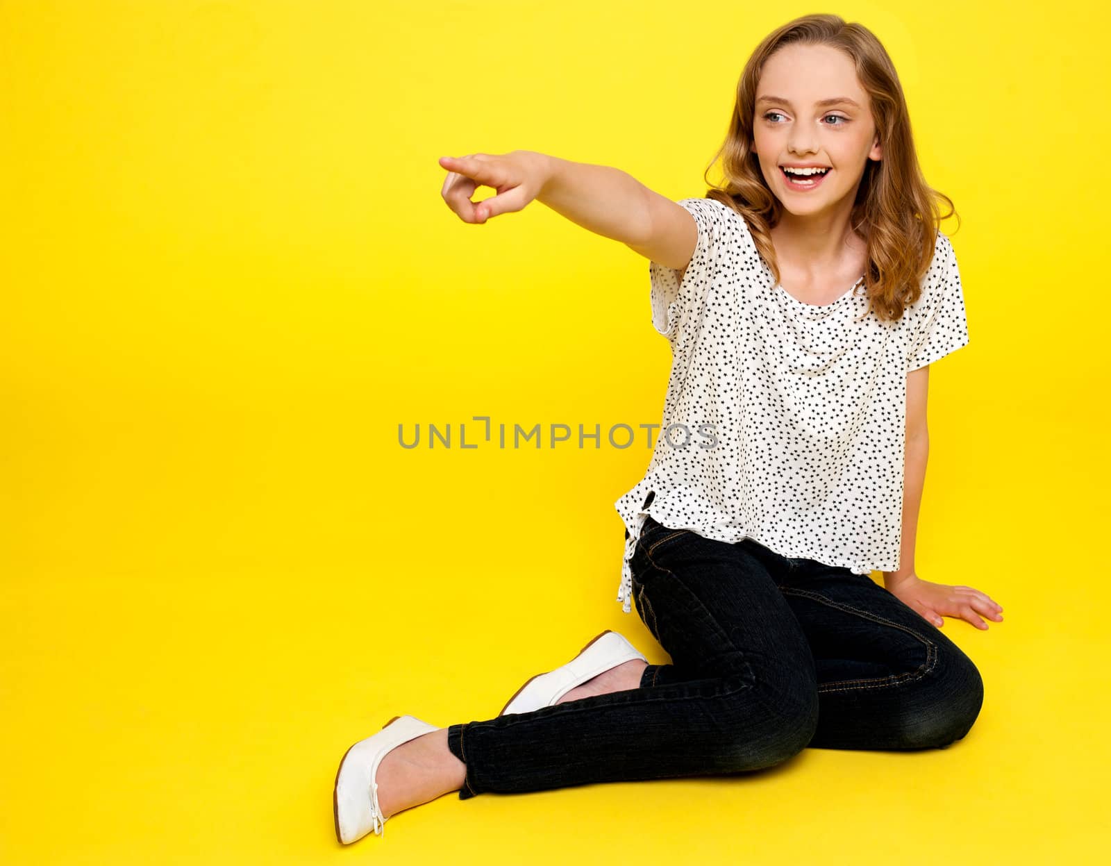 Smiling young girl pointing away. Sitting on floor