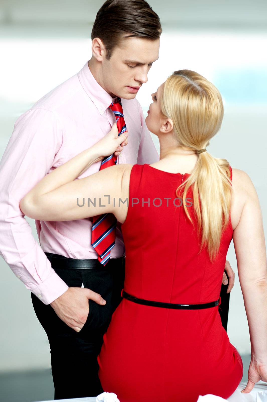 Woman pulling man from his tie. Feeling naughty. About to kiss inside office