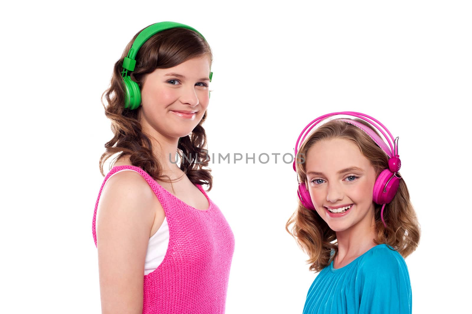 Elder and younger sisters listening to music through headphones against white background