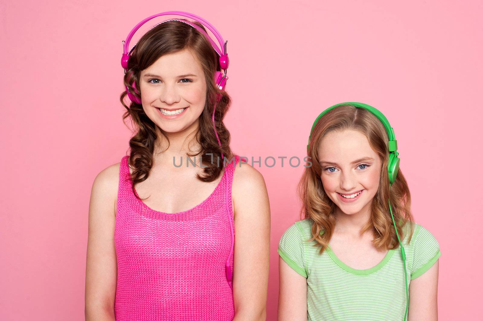 Smiling girls posing with headphone isolated on pink background