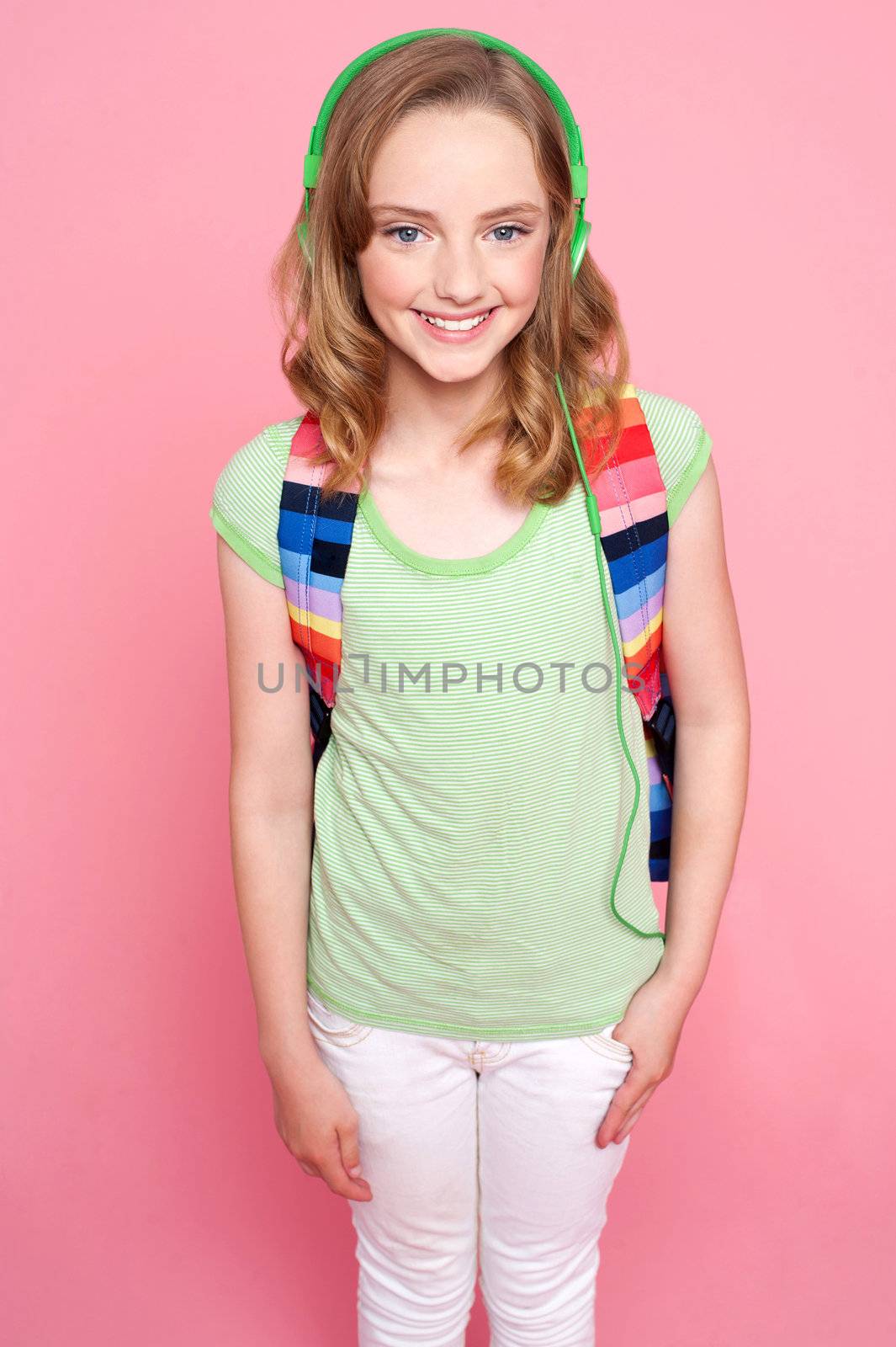 Cute girl with backpack and headphones smiling at camera in isolation