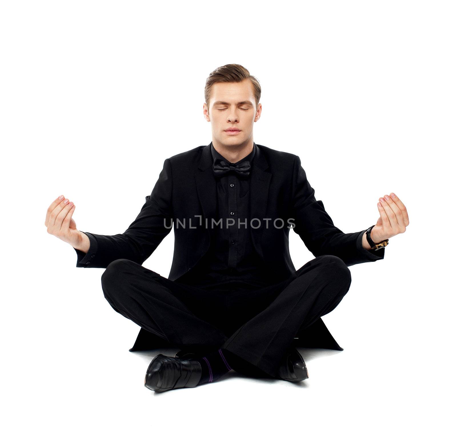 Smart young man in party wear doing yoga. Seated on floor in lotus pose