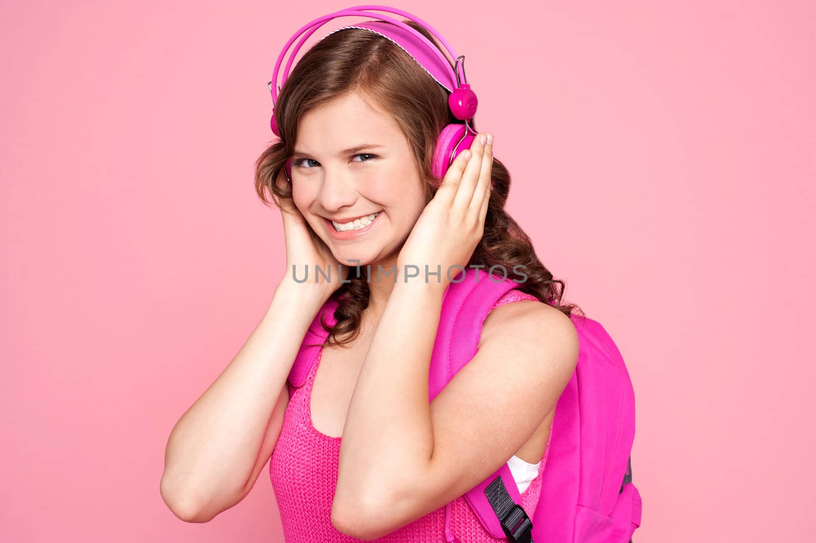 A beautiful young schoolgirl listening to music isolated over pink background