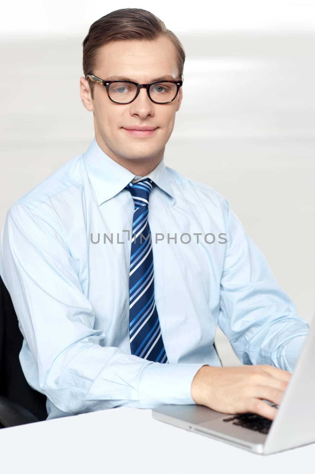 Man sitting on chair using laptop in office. Smiling at camera