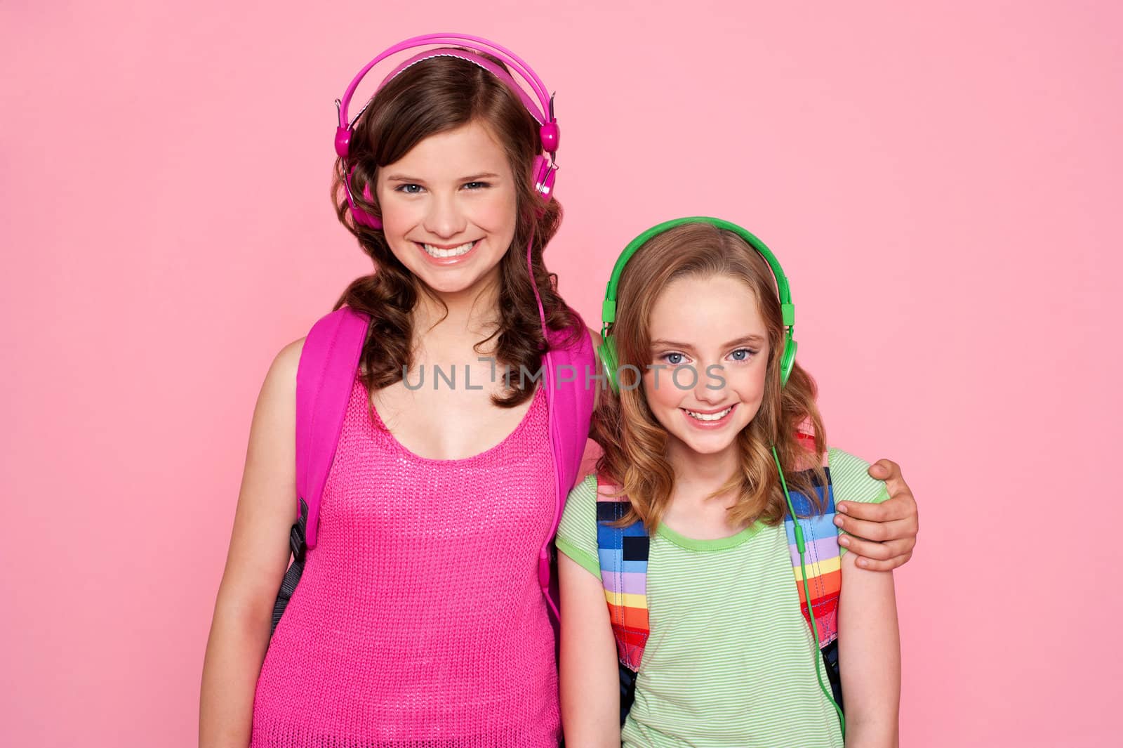 Sisters standing together and enjoying music isolated over pink background