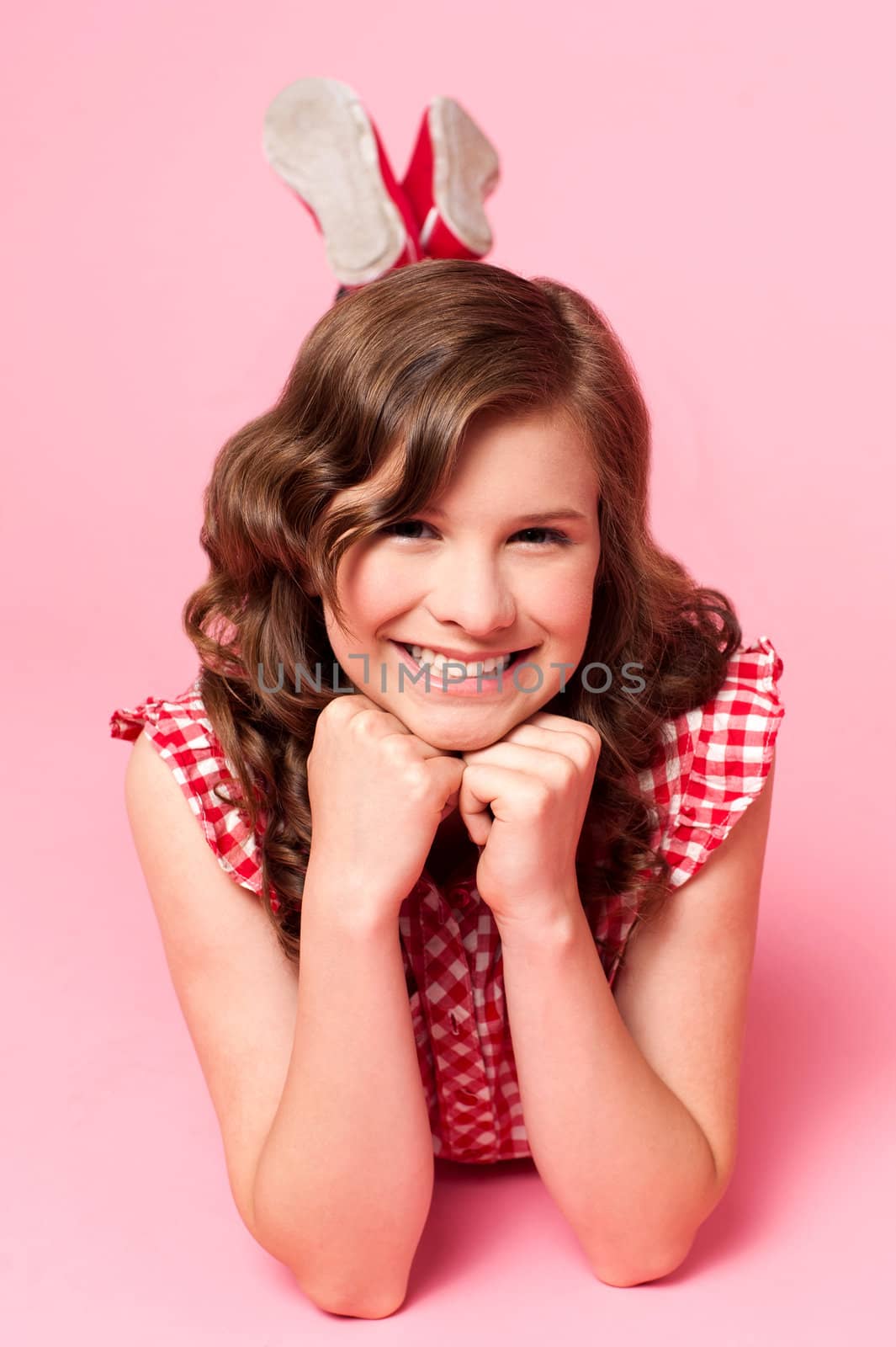 Happy young girl lying on floor. Hands on chin. All on pink background