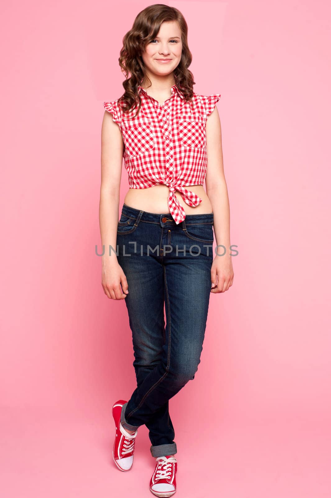 Pretty teenager standing with crossed legs. Full length shot over pink background
