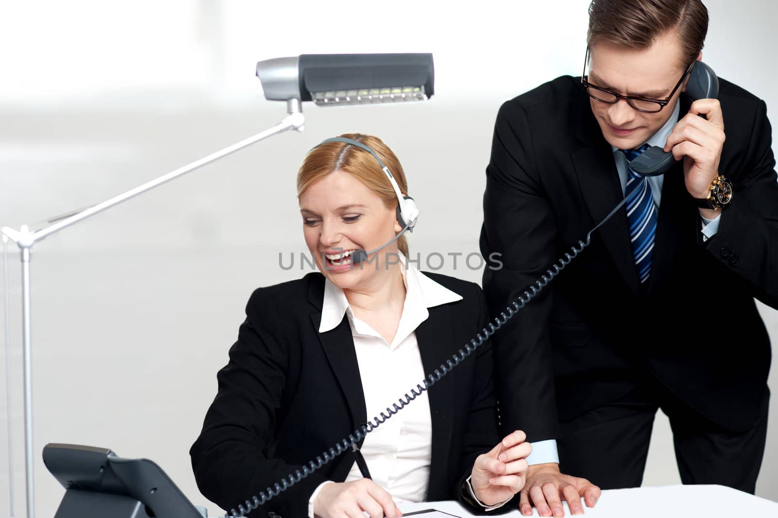 Male executive attending clients call while female secretary enjoys the conversation