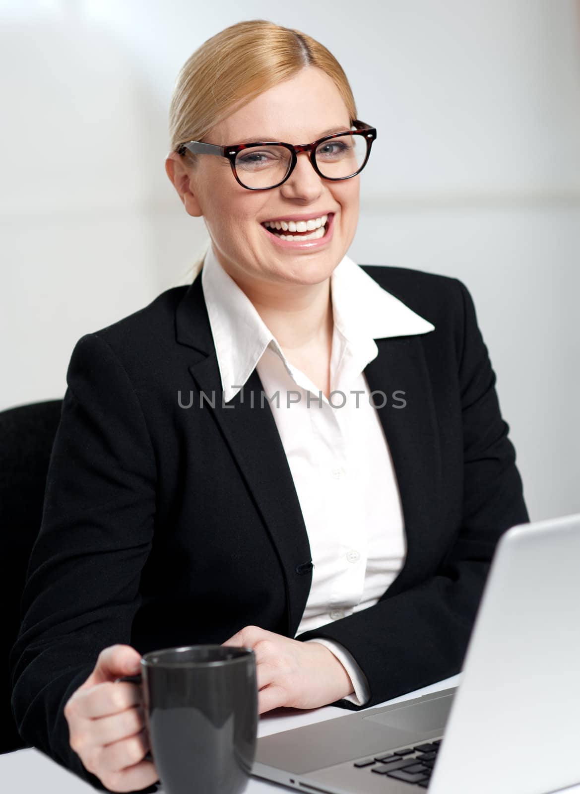 Beautiful smiling businesswoman holding coffee cup in front of laptop