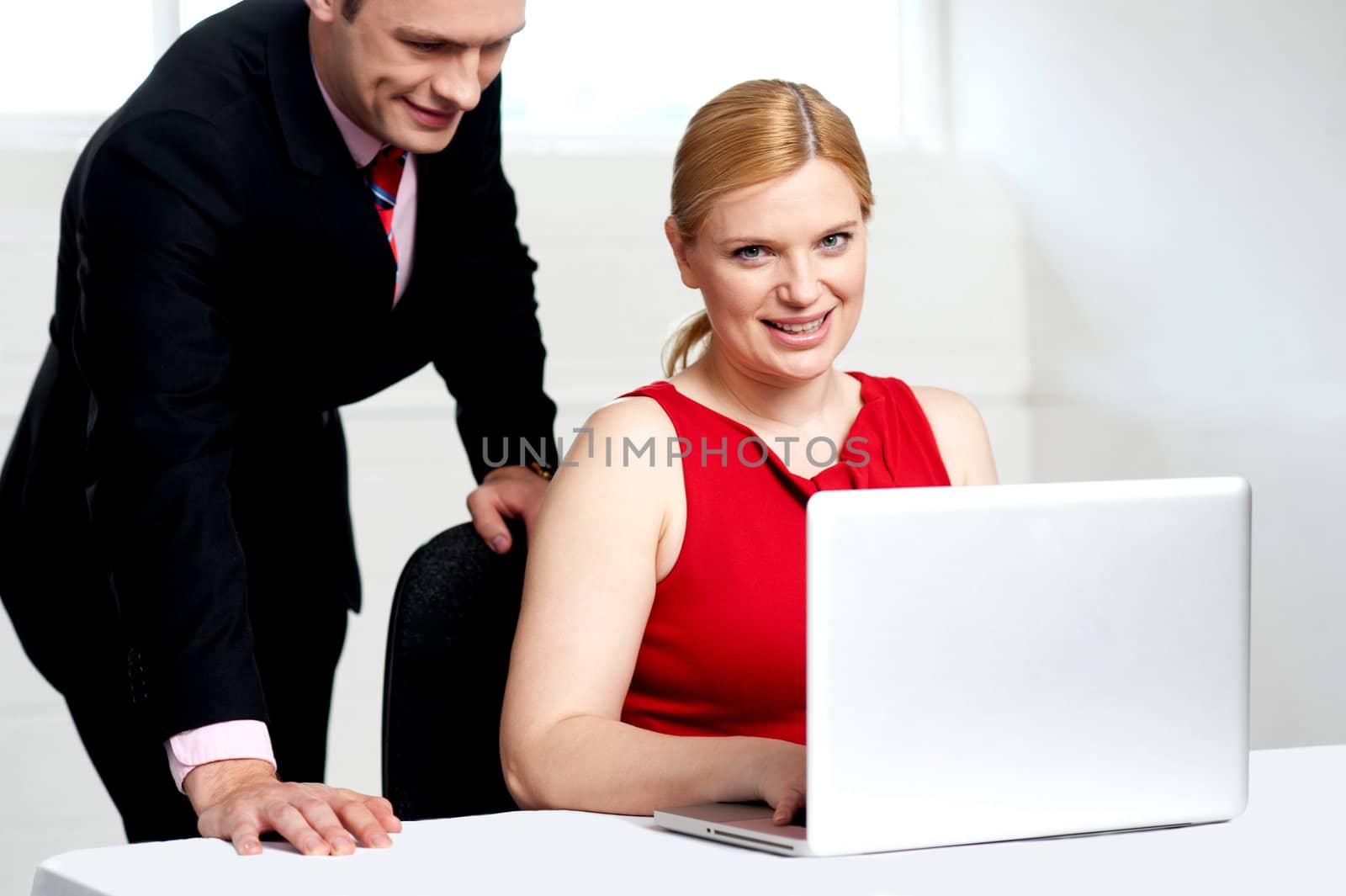 Trendy female boss working on laptop with man assisting