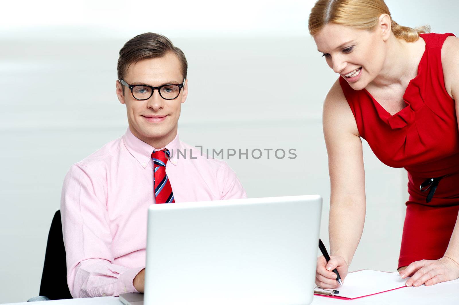 Woman writing information from laptop while businessman looking at camera