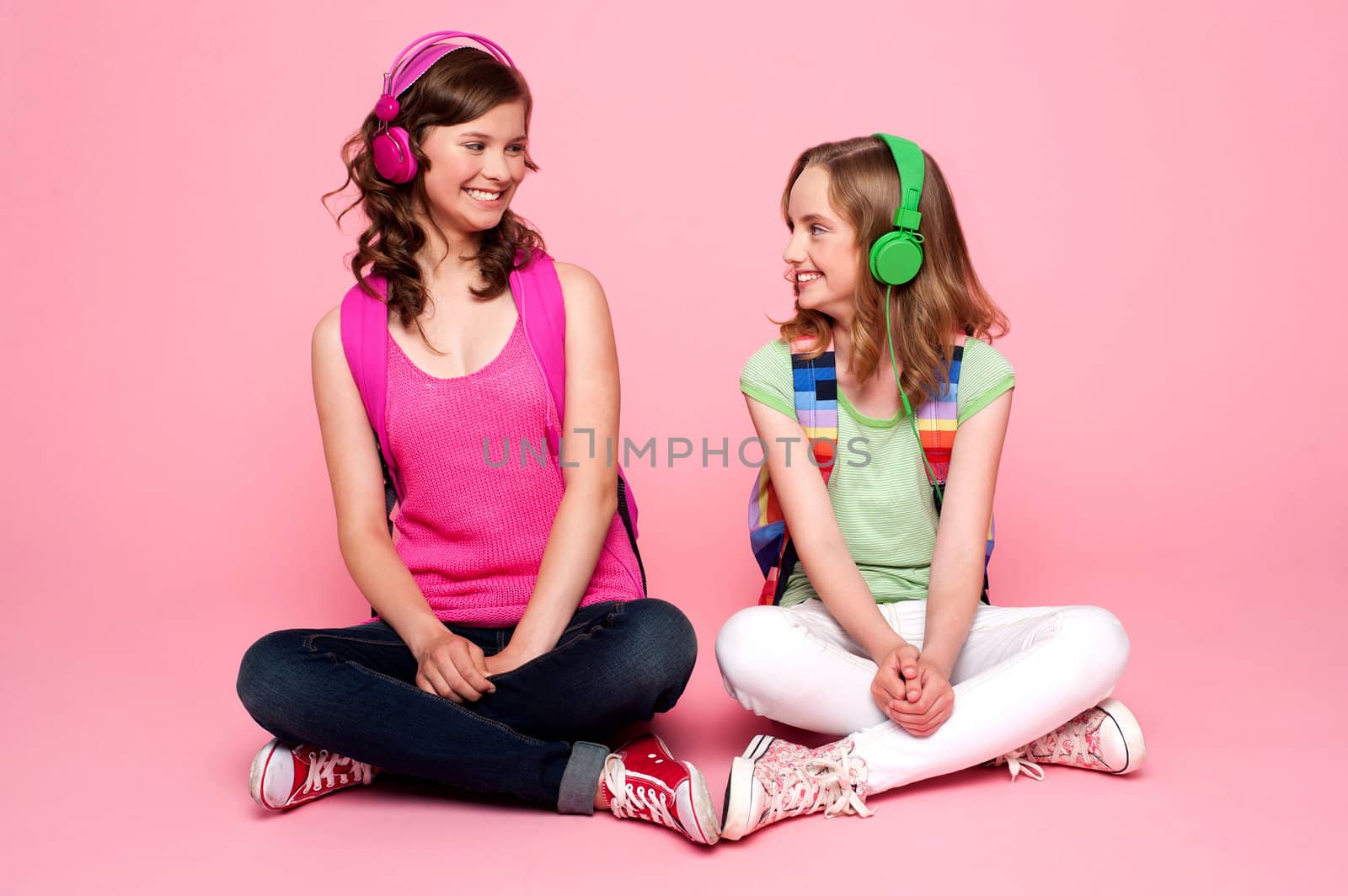 Seated beautiful teenagers looking at each other. Pretty schoolgirls