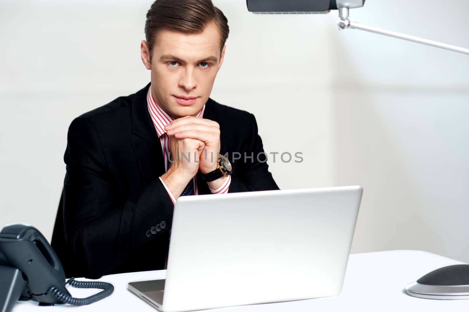 Portrait of businessman sitting in front of laptop with hands on chin