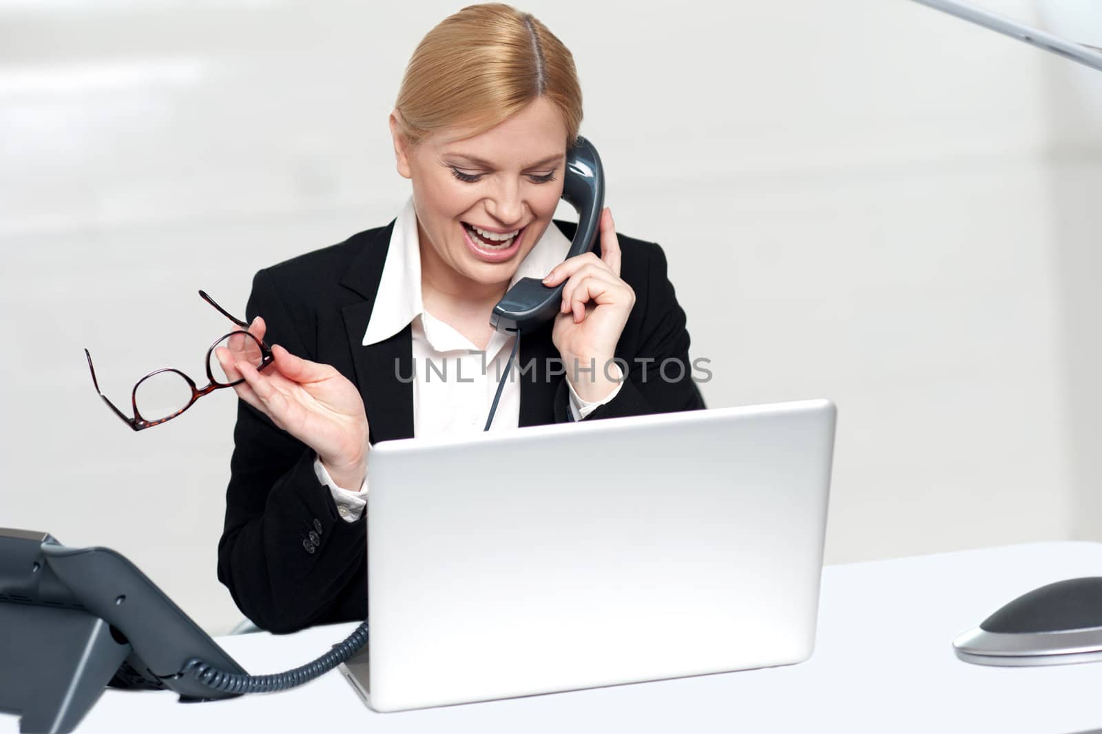 Woman talking on phone holding eye glasses looking into laptop