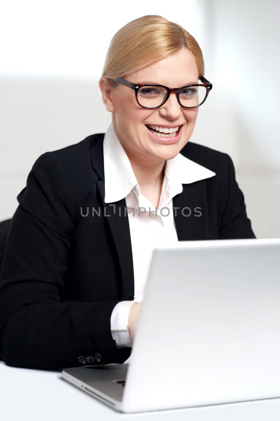 Smiling young female executive at work desk operating on laptop