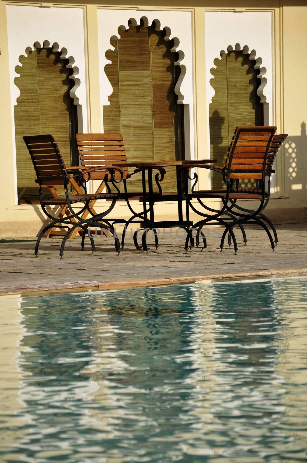 Wooden chairs by a swimming pool around architecture reflecting the ancient heritage of Udaipur, India