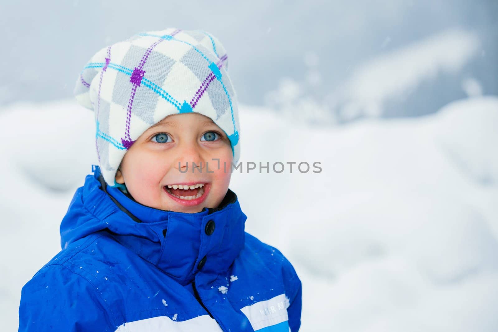 Smiling happy boy having fun outdoors on snowing winter day in Alps playing in snow.