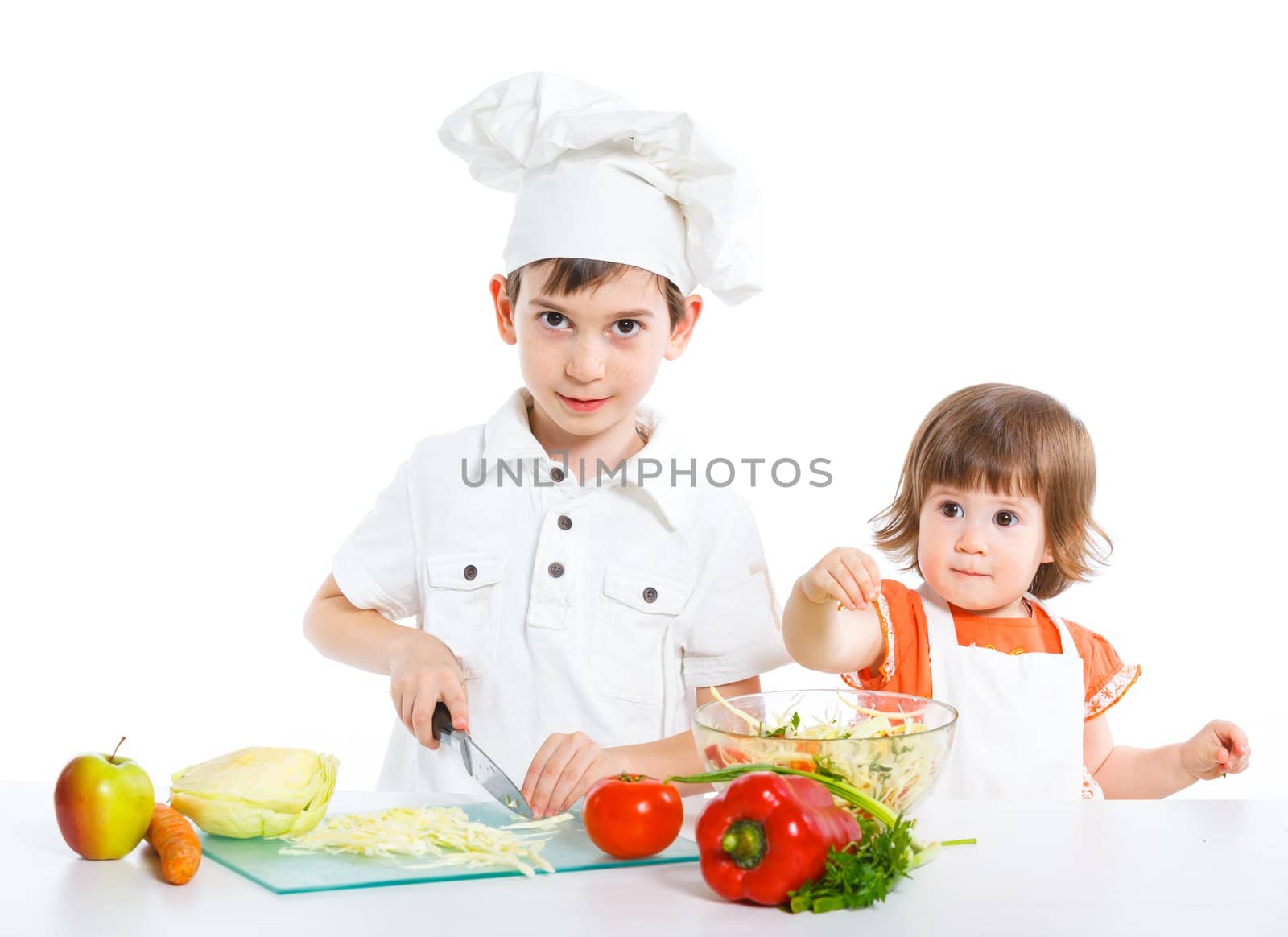 Two smiling kids mixing salad, isolated on white