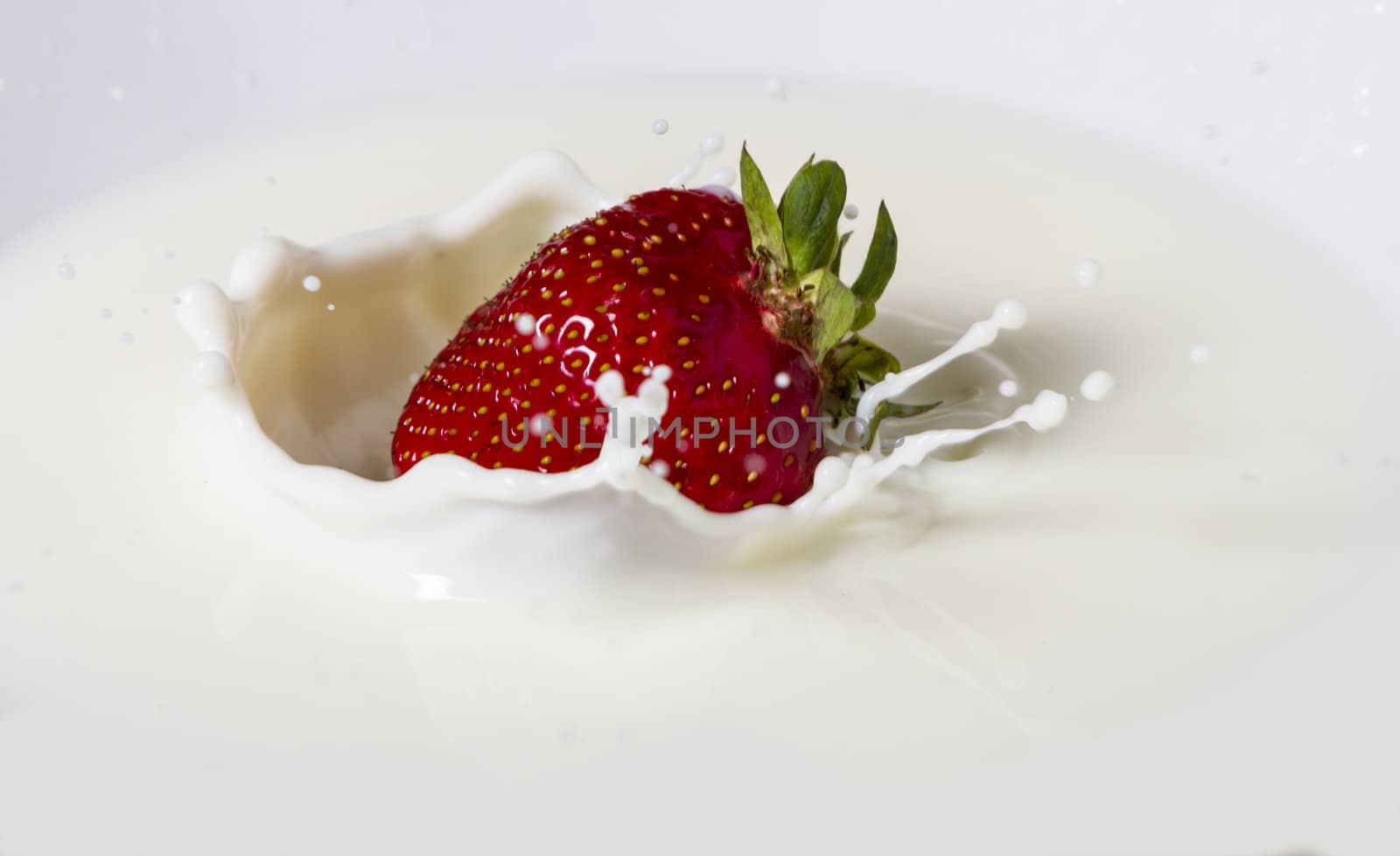 red, fresh strawberry falling in plate with milk