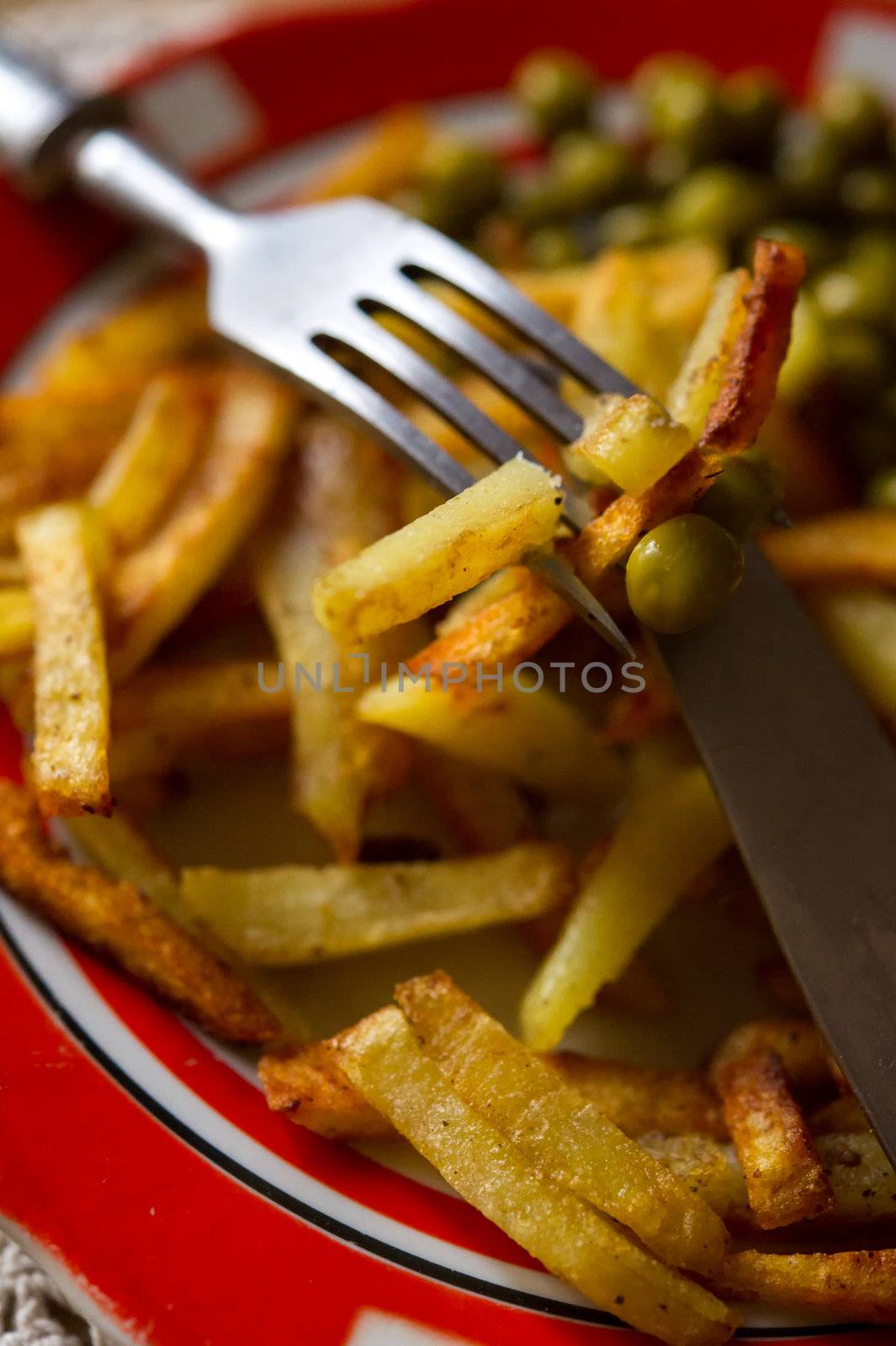 French fried potatoes with green peas on a plate served with fork and knife