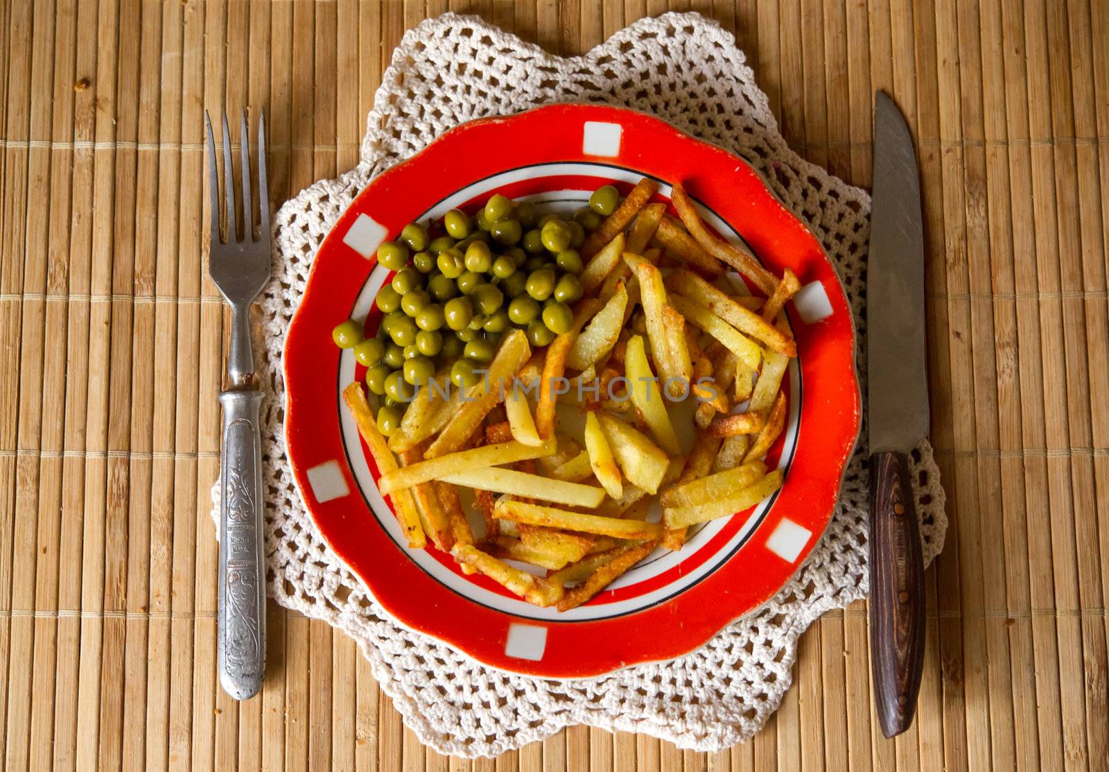 French fried potatoes with green peas on a plate served with fork and knife