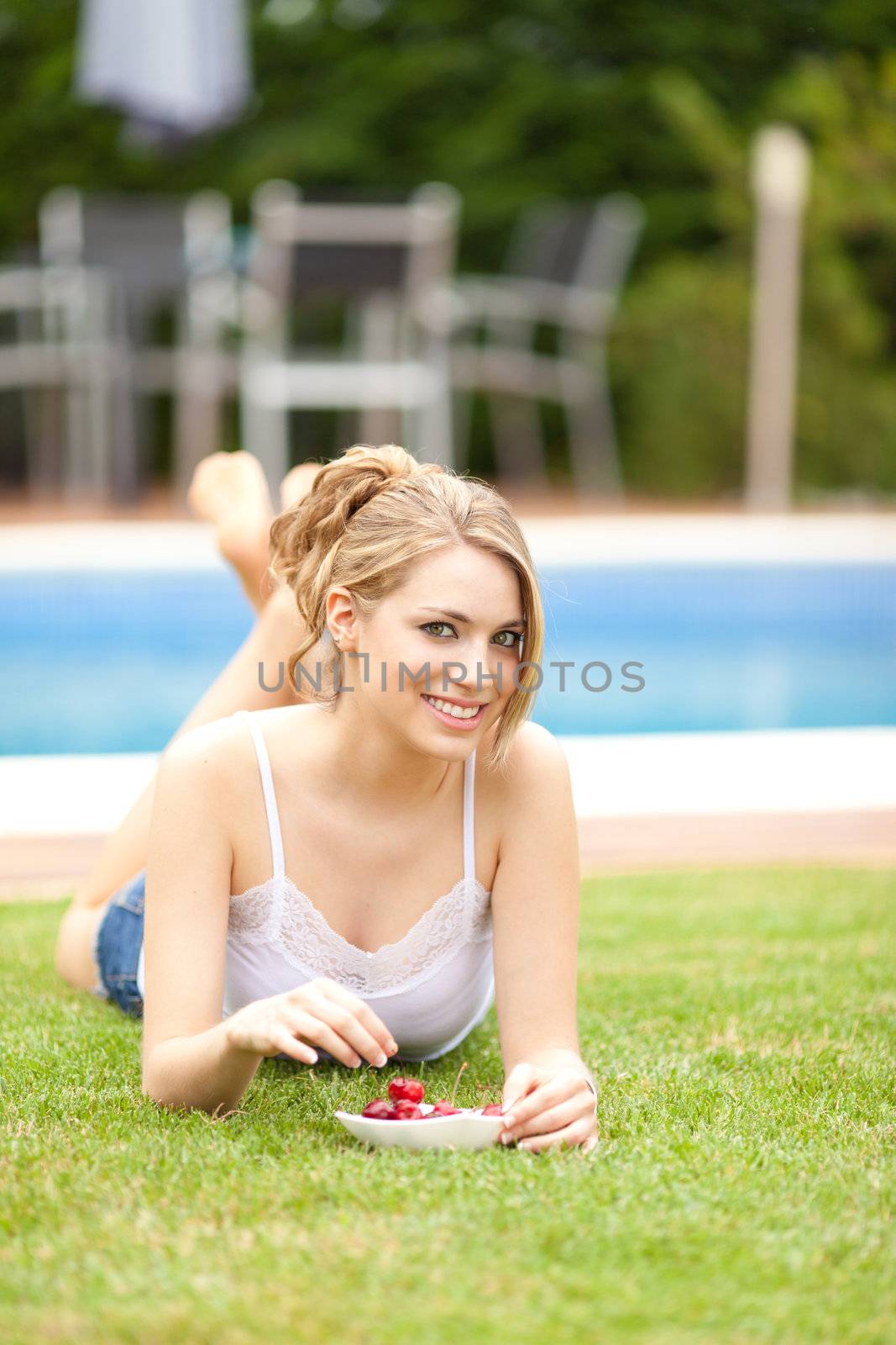 young beautiful blonde girl eating cherries on the grass