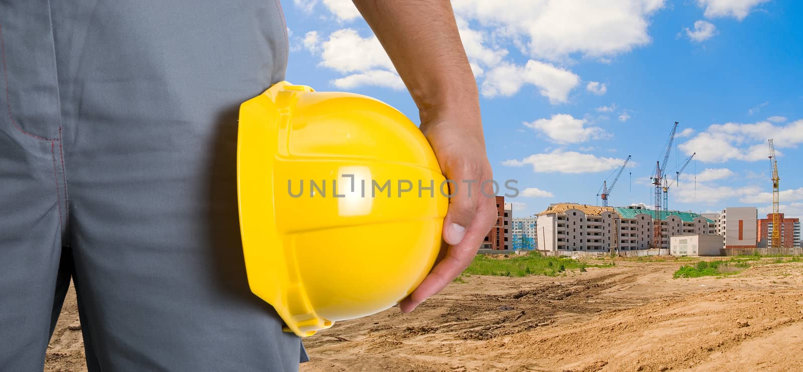 Closeup  of yellow helmet at builder hands on building background