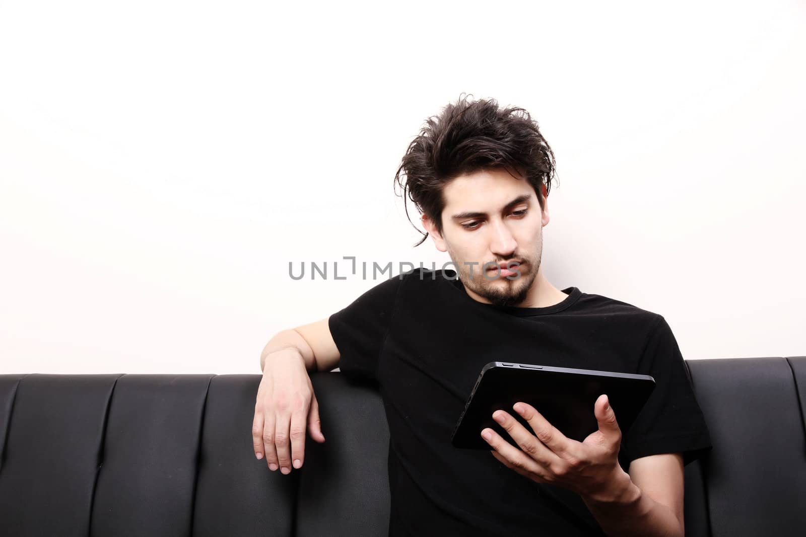 A young hispanic man sitting on the sofa holding a Tablet PC.