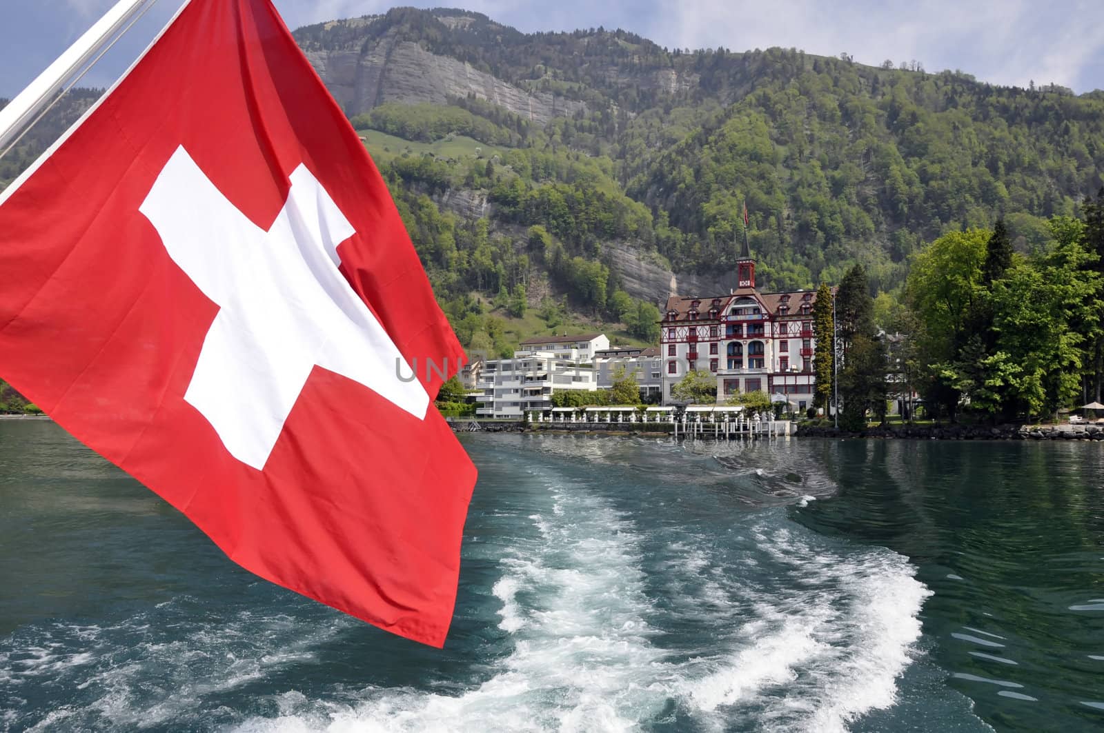 Swiss flag in boat, during summer. Lake and mountains in the back.