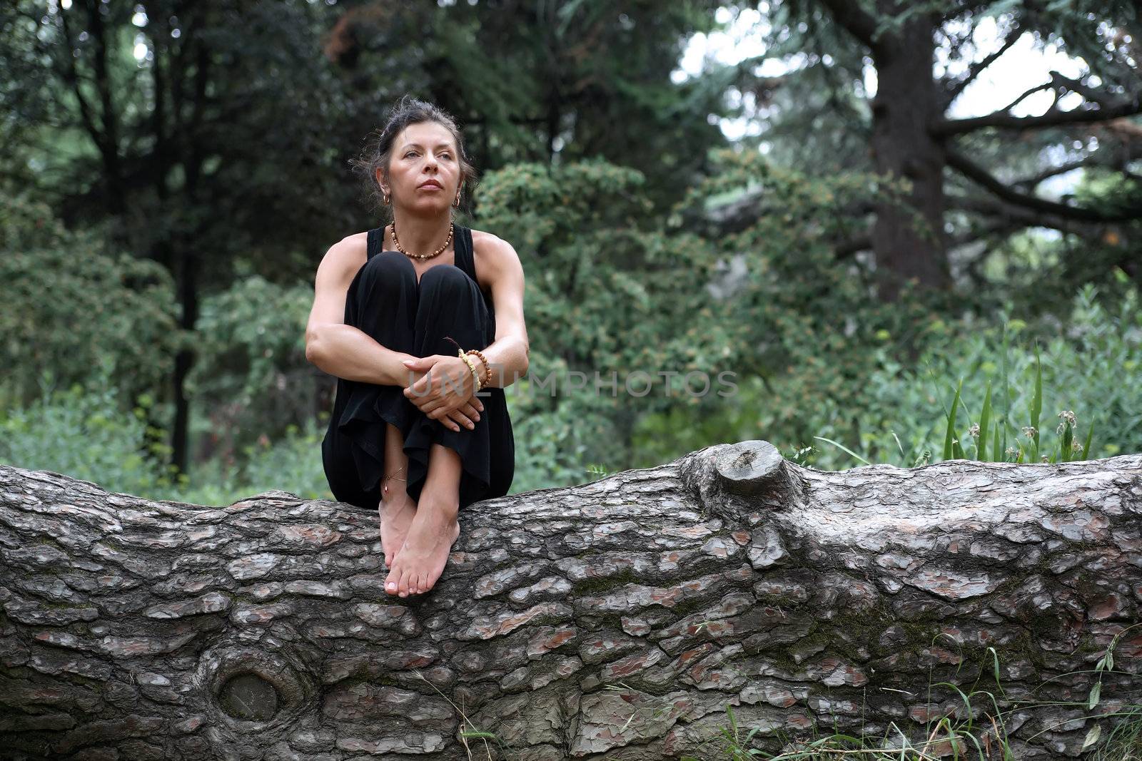 Portrait of strength attractive mature woman in black sitting on wooden log in forest