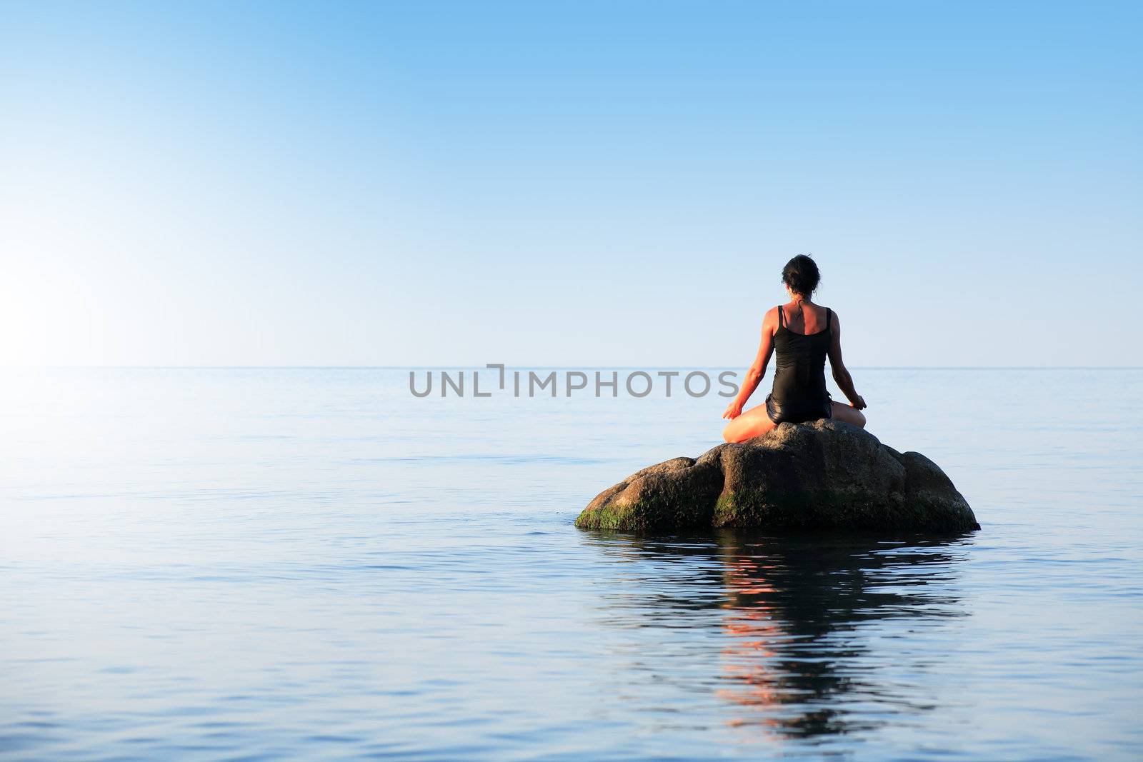 Svelte adult woman doing yoga on big stone in the sea