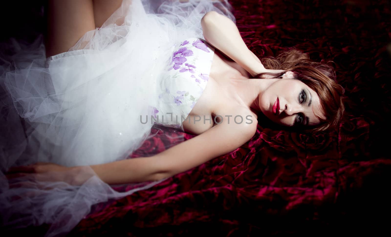 Beautiful and sensual redheaded woman lying on a bed of roses