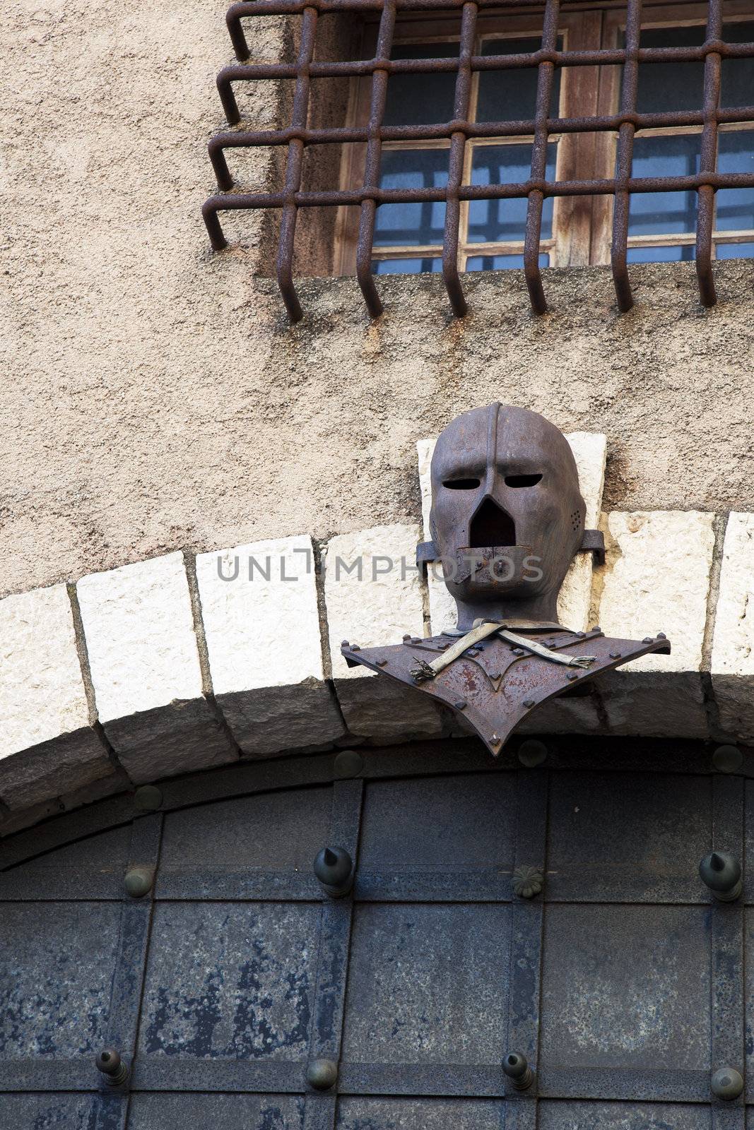 Rusted mask mounted over old doors with grated window above