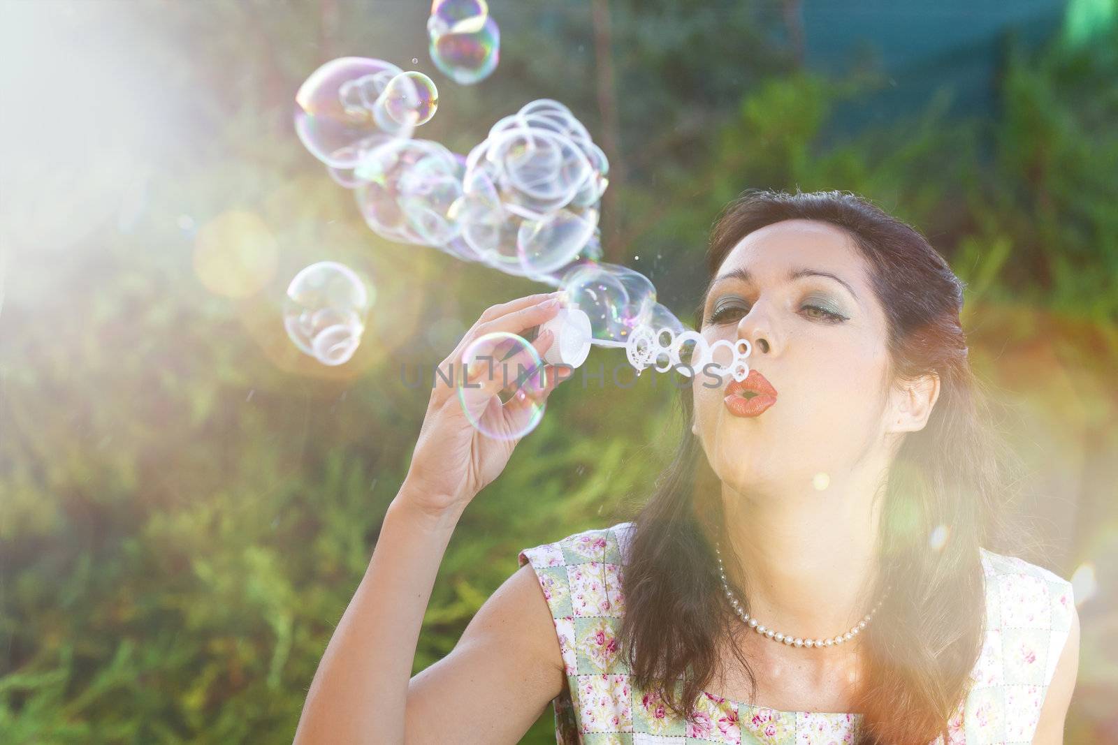 romantic young woman inflating colorful soap bubbles in spring park