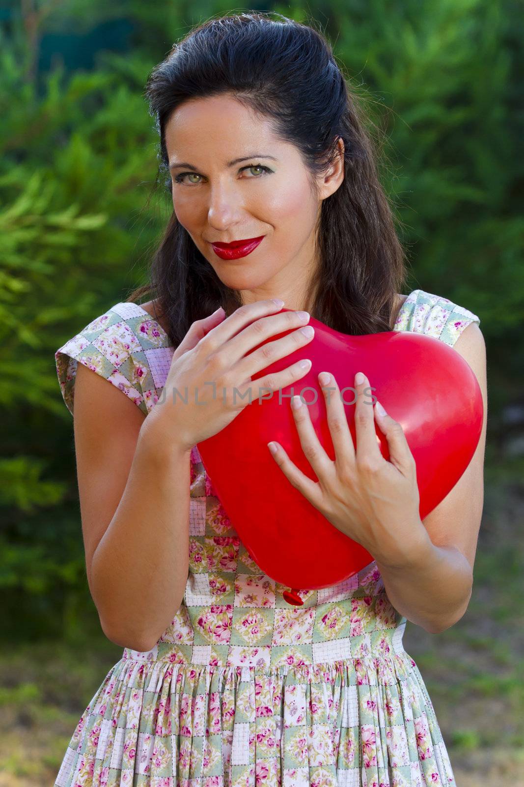 Attractive happy smiling brunette woman hugging one red valentine heart, woman on park, concept of valentine's day