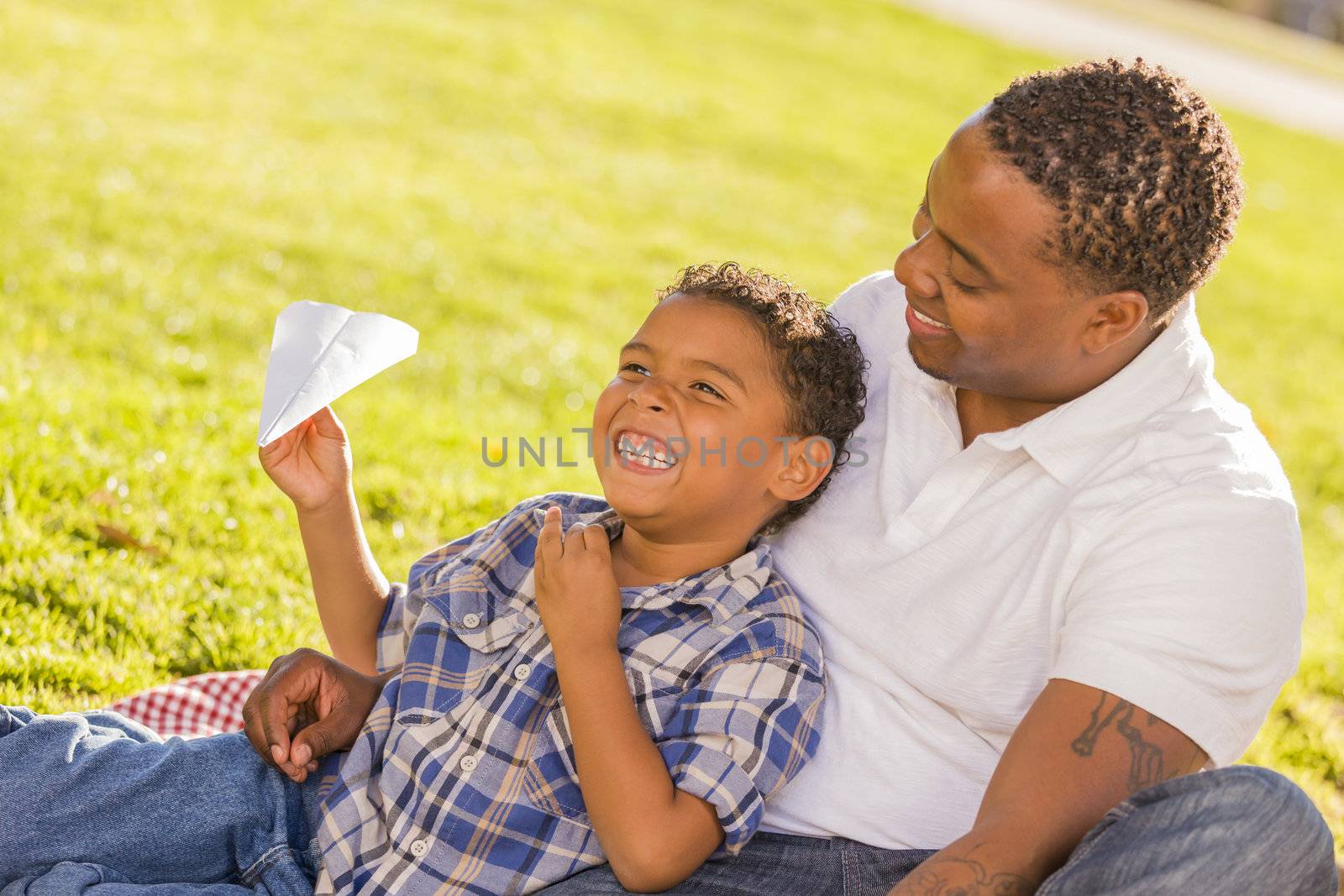 Happy African American Father and Mixed Race Son Playing with Paper Airplanes in the Park.
