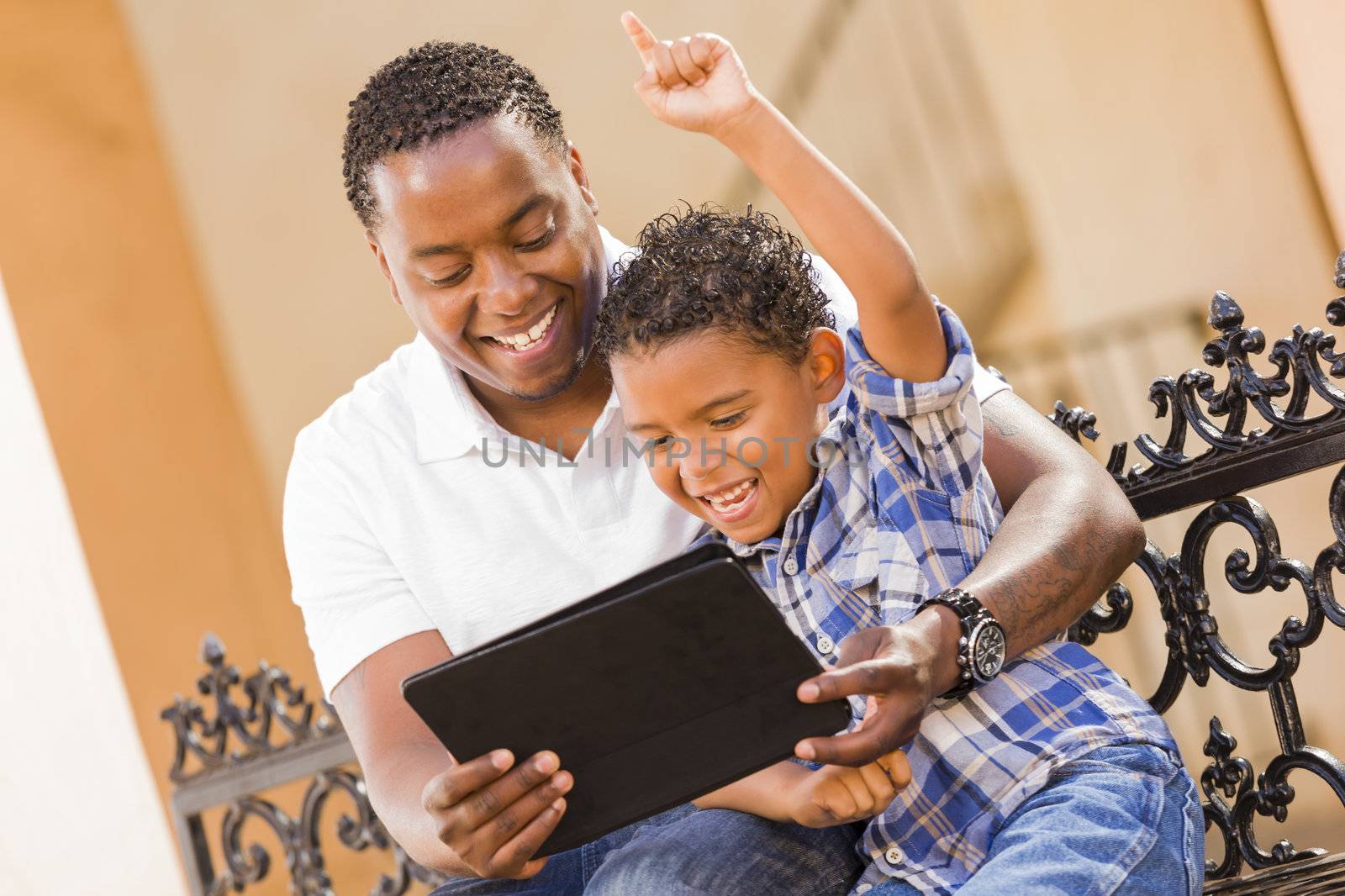 Happy African American Father and Mixed Race Son Having Fun Using Touch Pad Computer Tablet Outside.