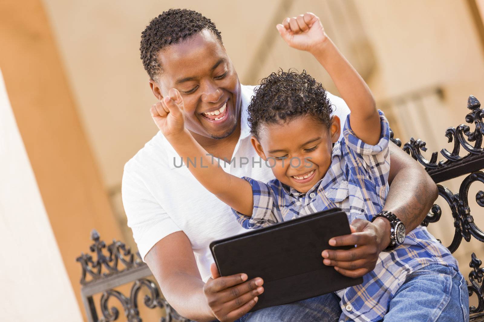 Happy African American Father and Mixed Race Son Having Fun Using Touch Pad Computer Tablet Outside.