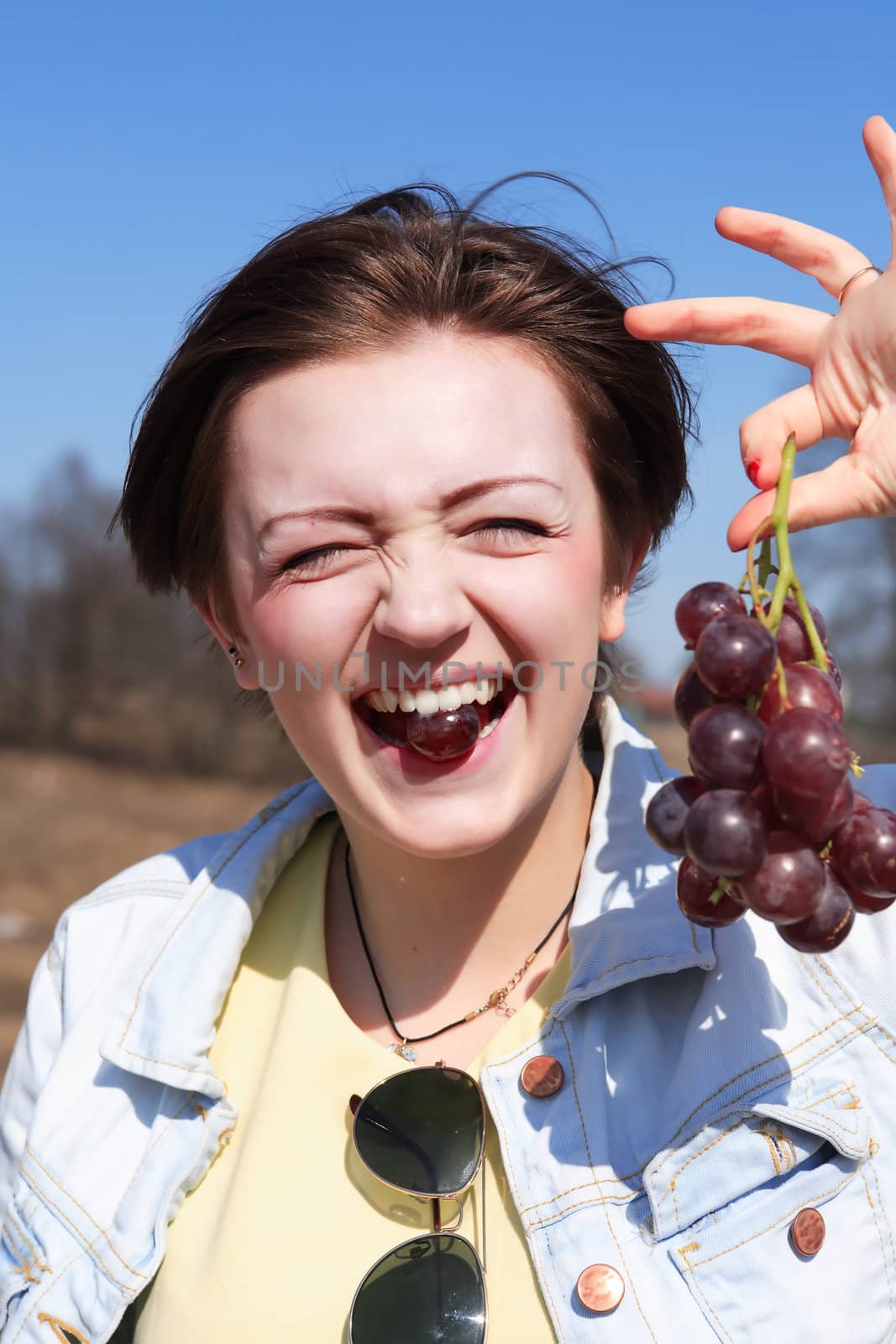 Beautiful young girl eating red grapes outdoor on blue sky background