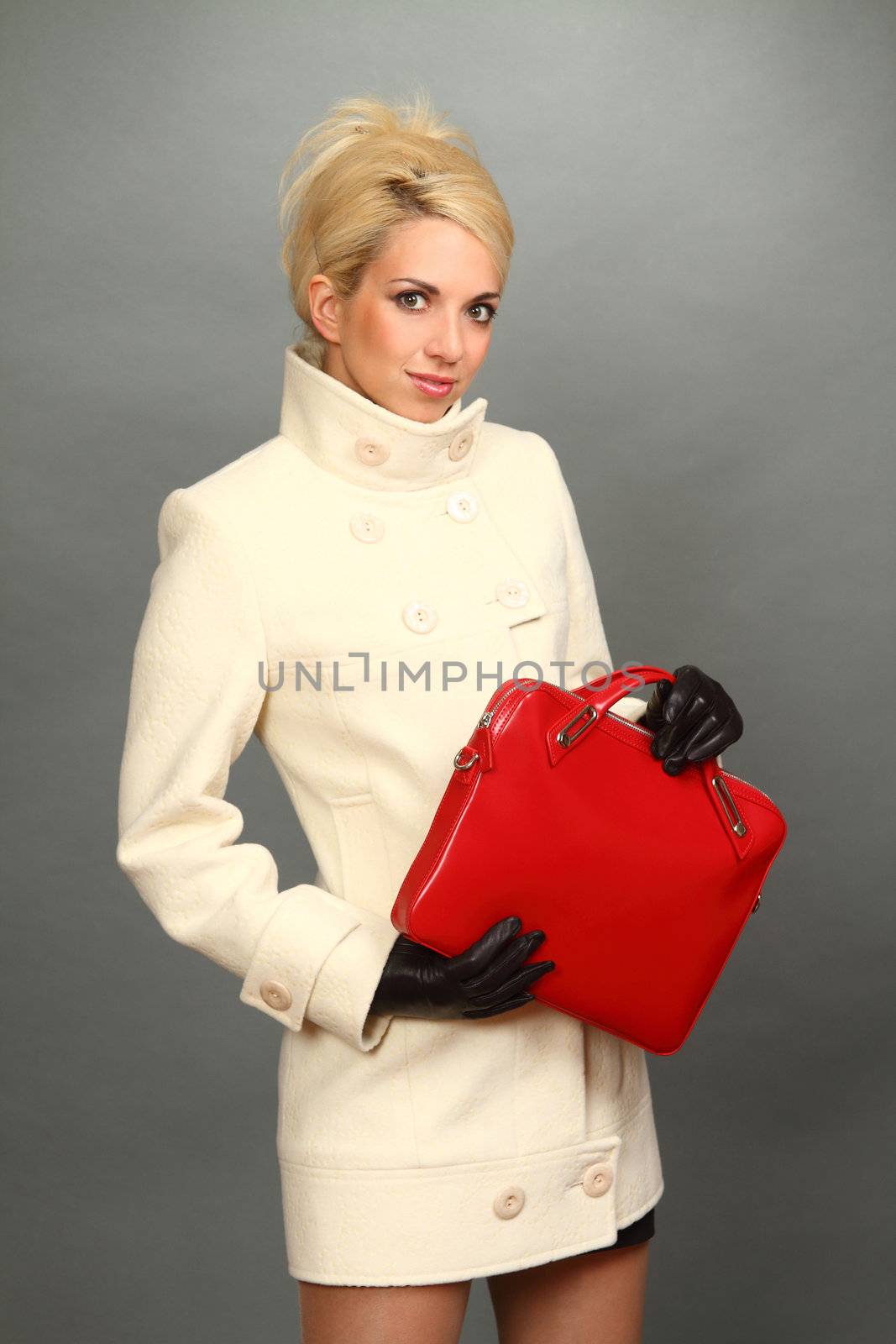 The beautiful blonde in a light coat and black leather gloves with a red handbag in hands