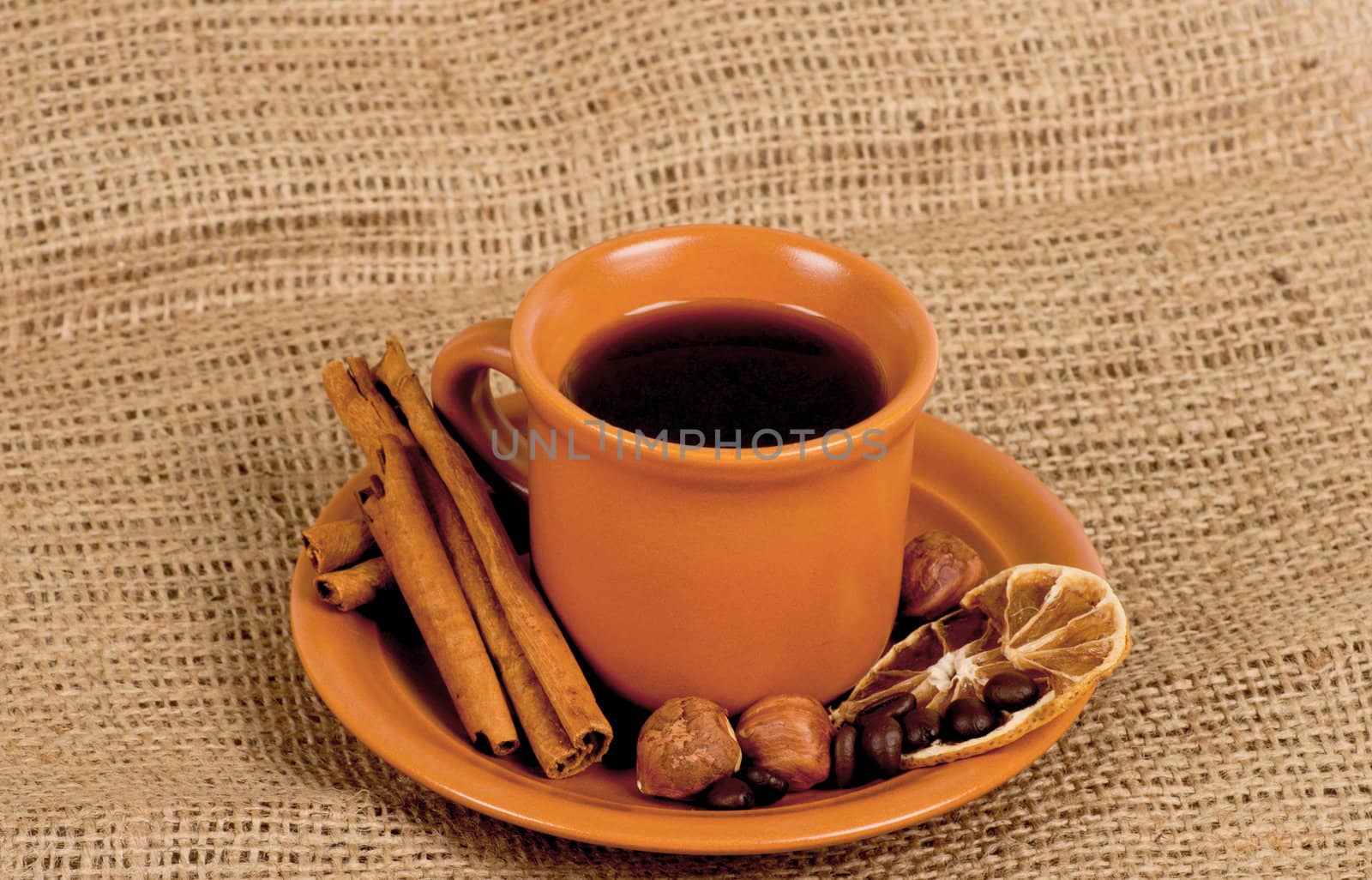 Closeup shot of freshly prepared cup of italian espresso with cinnamon, coffe beans, nuts and lemon over sacking