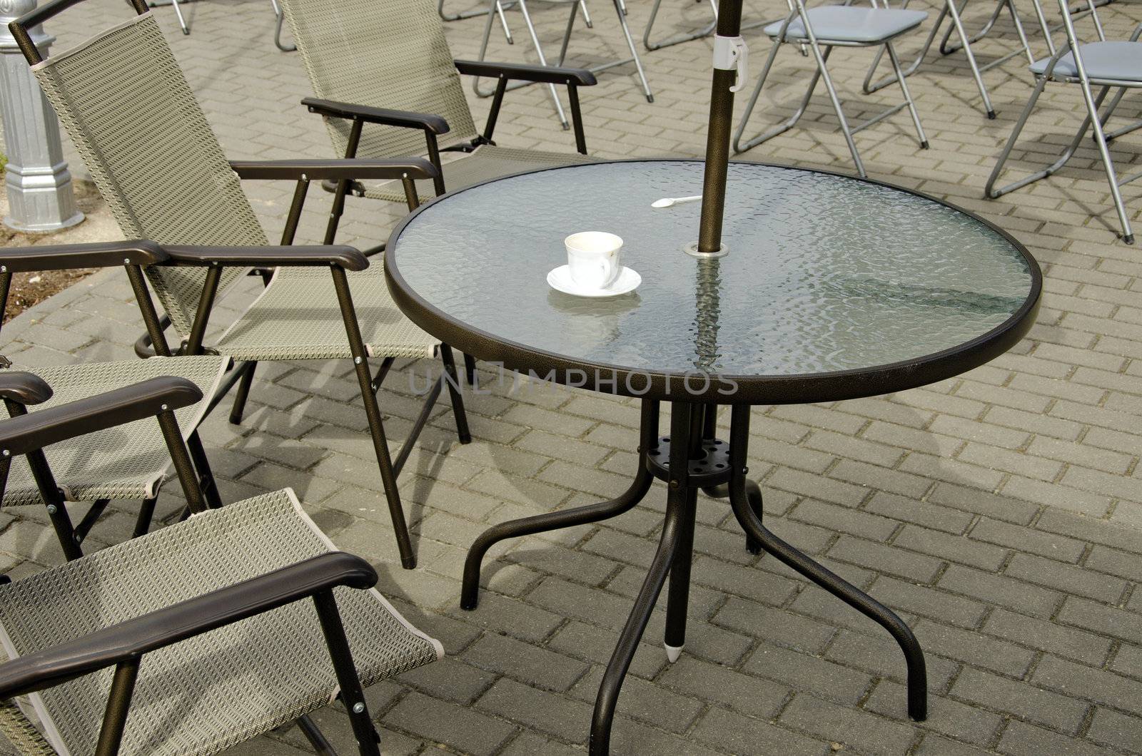 Empty coffee cup on table and chairs on pavement. Outdoor cafe.