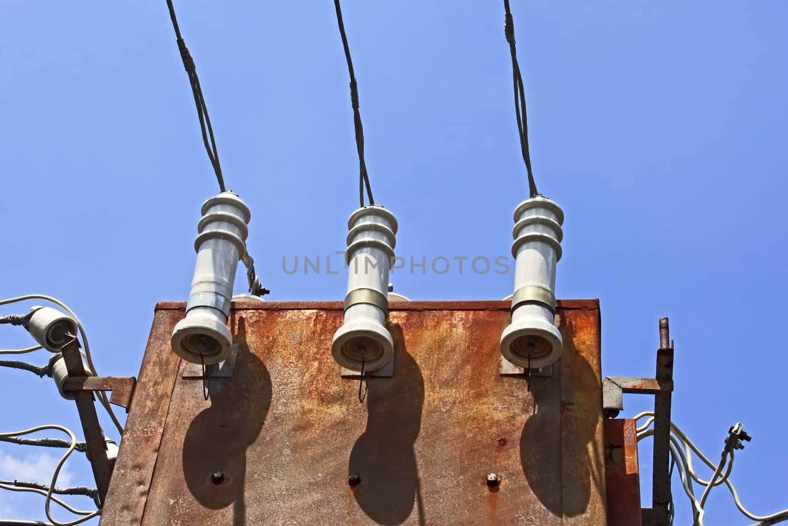 Electric insulators and wires on the old three-phase electrical transformer on a background of blue sky