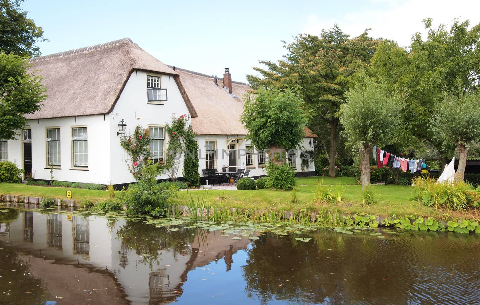 Luxury house with a thatched roof and a garden with drying laundry and reflection in the water.