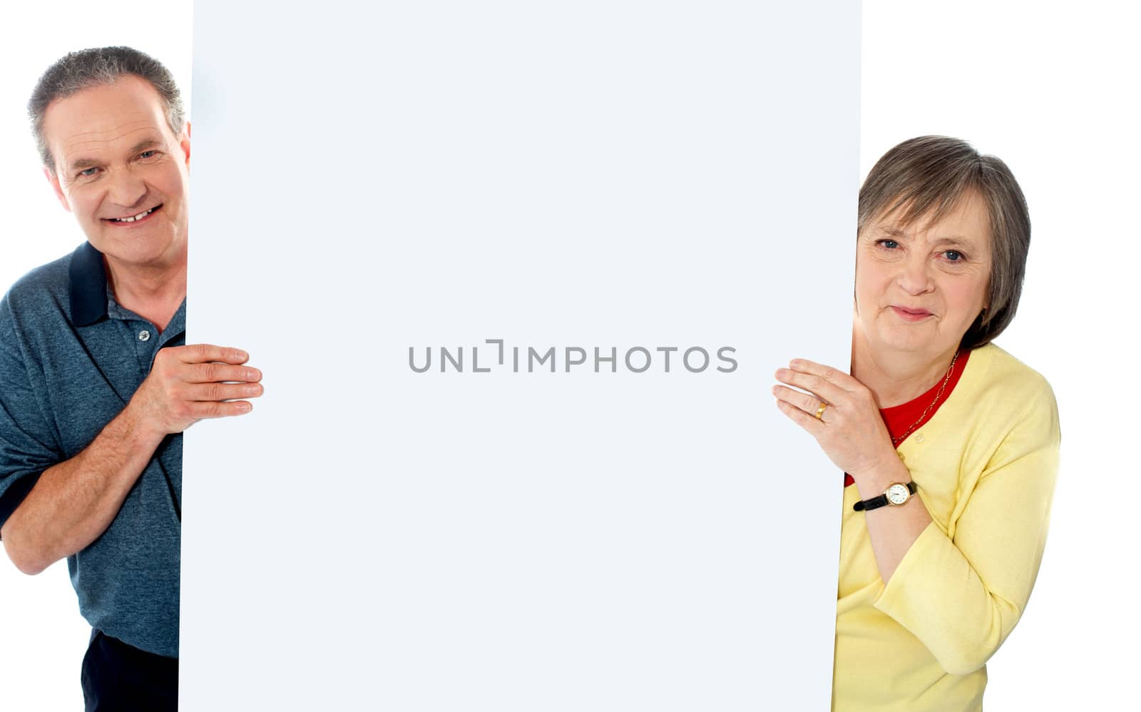 Senior couple standing behind blank billboard looking at camera