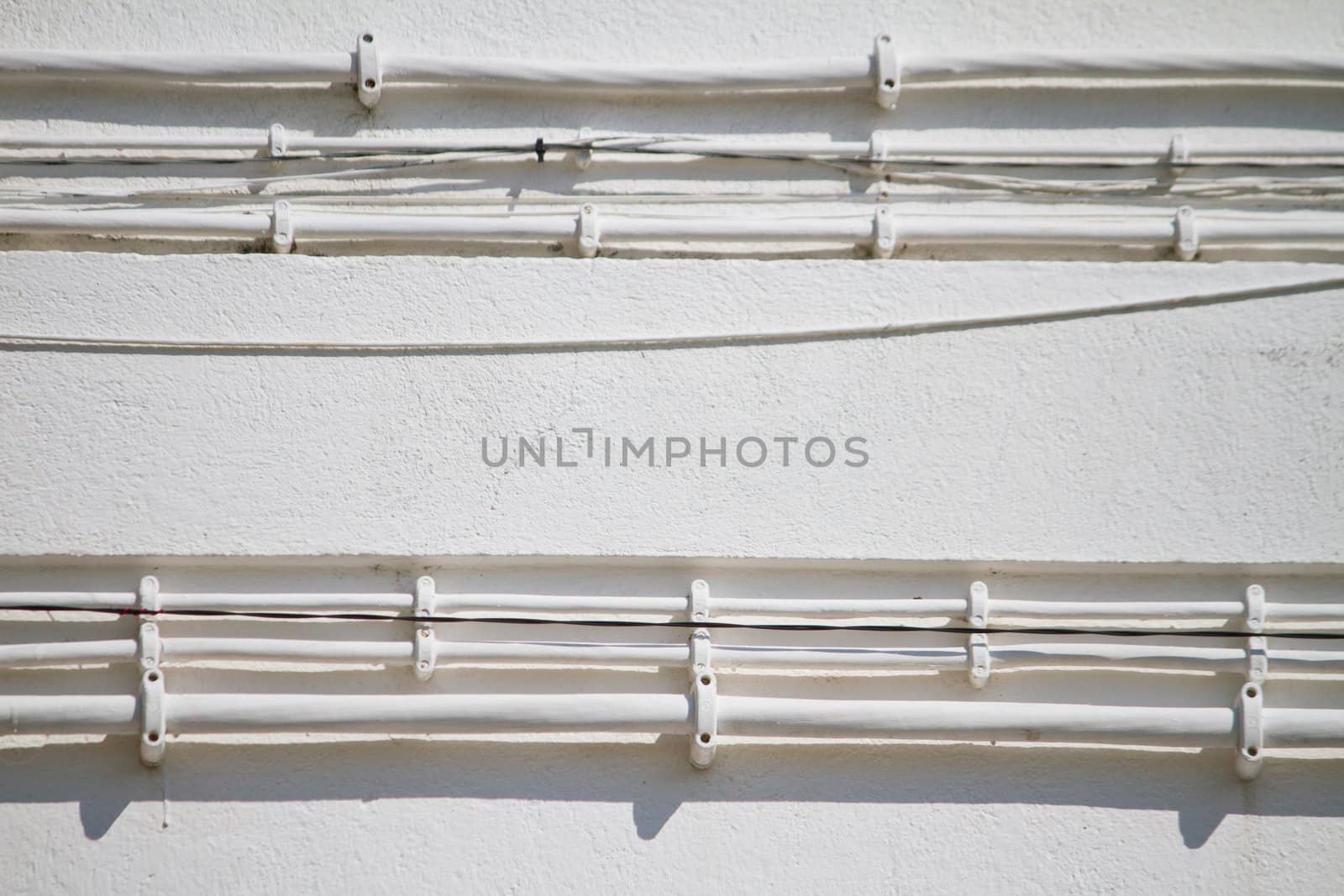 Close view of some old electricity cables attached to a white wall.