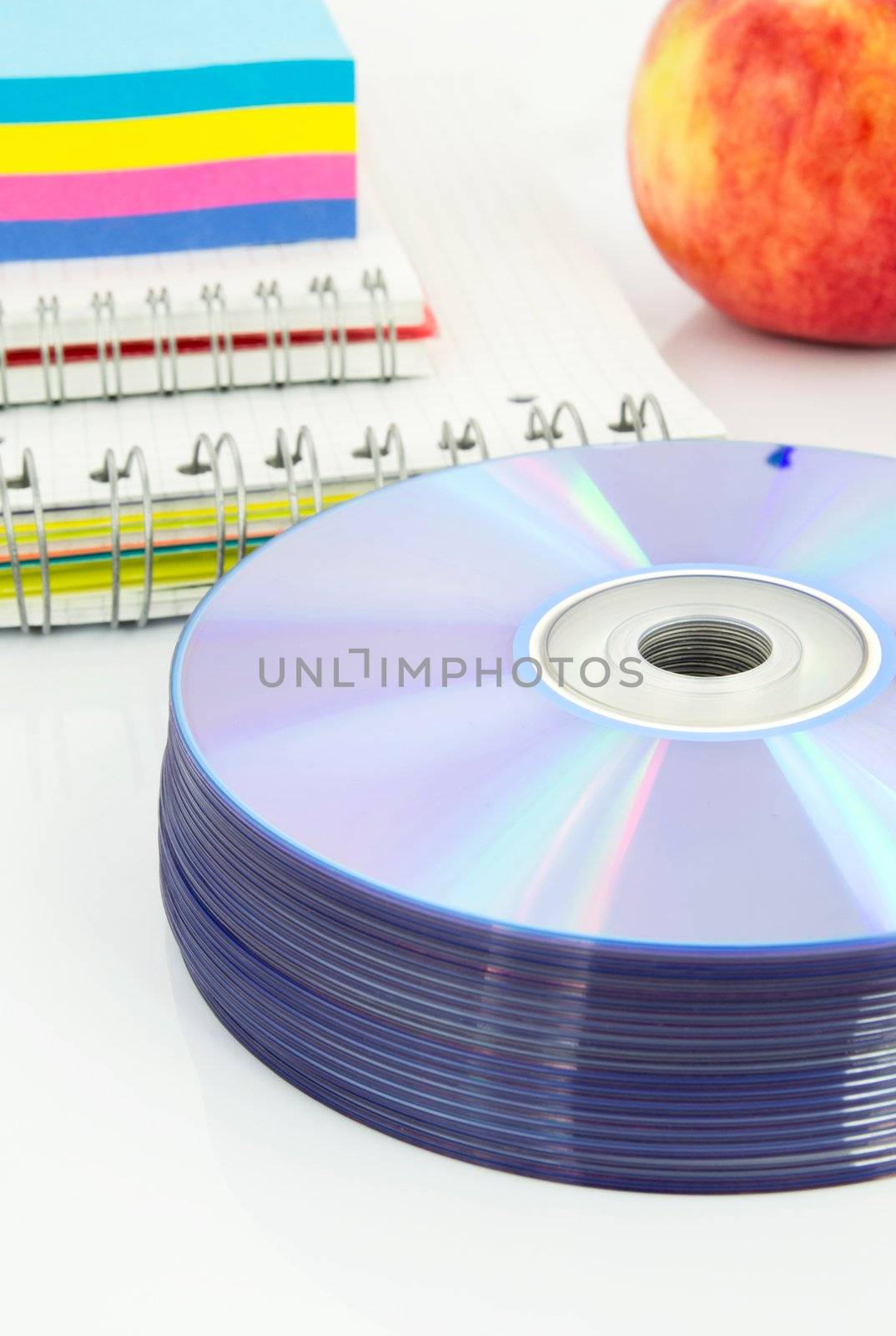 Compact discs, color paper, copybook, apple on white desk by simpson33