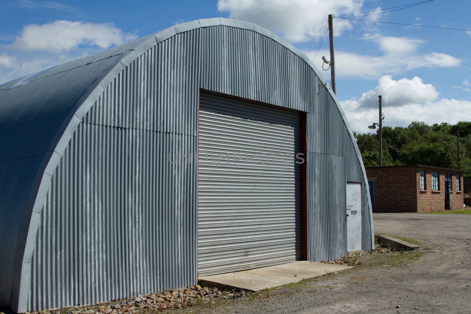 An industrial unit made from corrugated metal sheets with a roller shutter and door on rough ground.